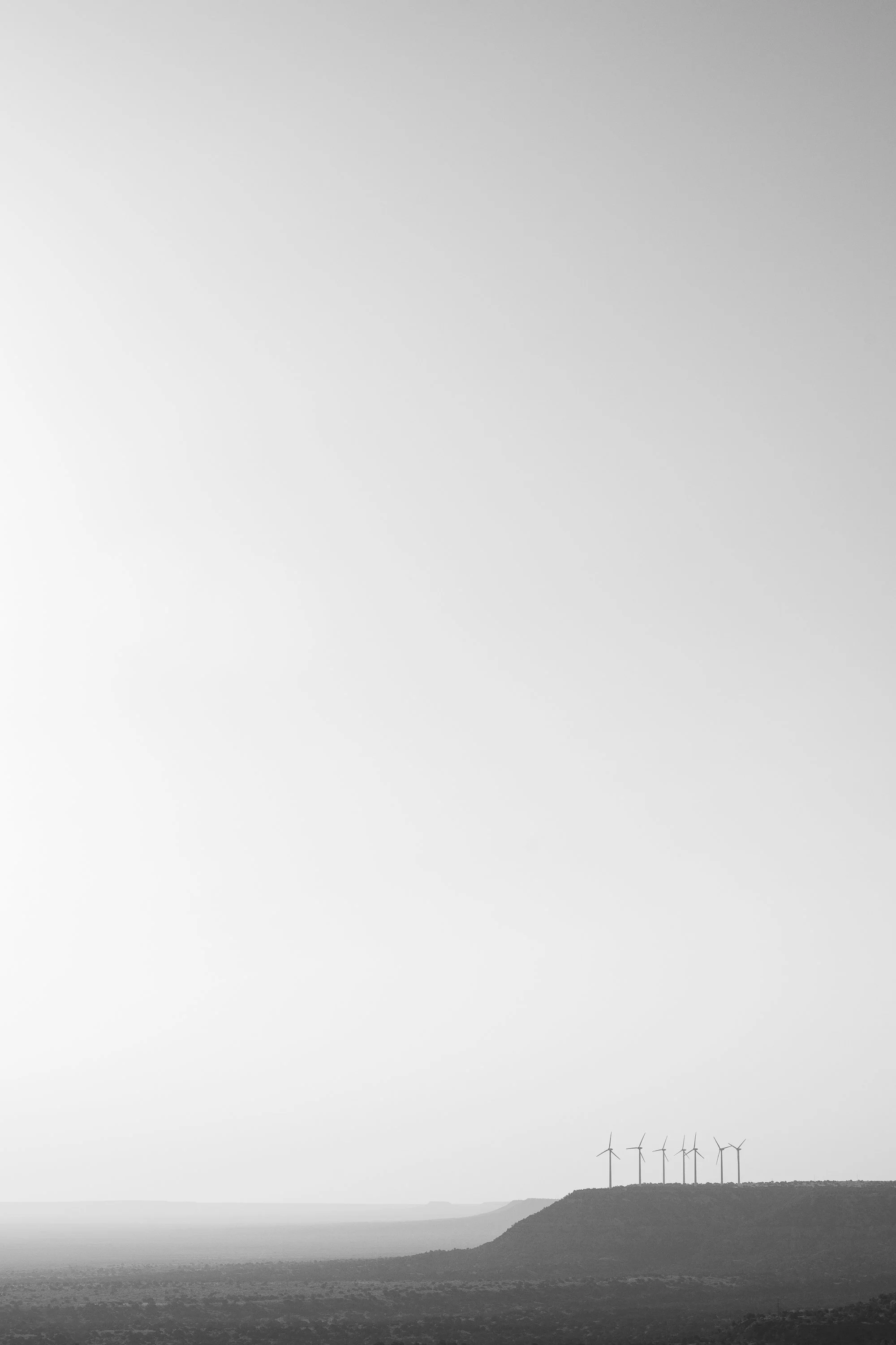 Minimal black and white photograph of a wind farm along the Llano Estacado horizon