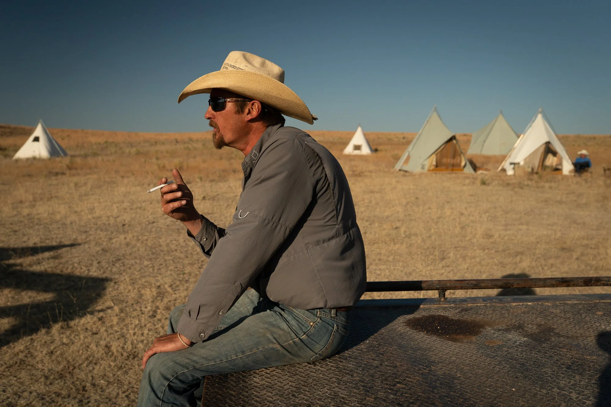 Cowboy sitting on a truck bed smoking near canvas tents at the 6666 Ranch in Texas.