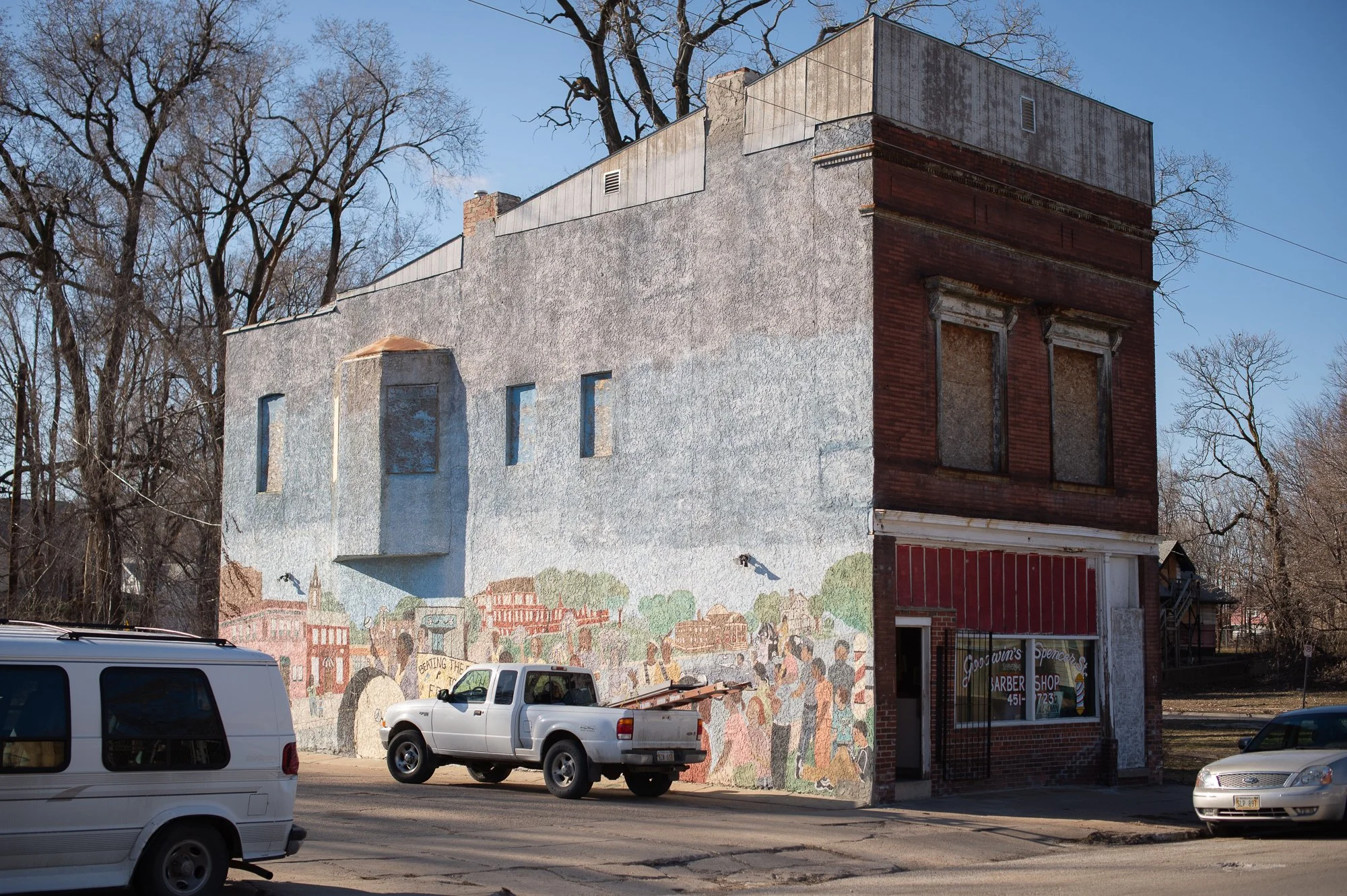 Exterior of an old Black barbershop building with mural and parked cars in a small American town