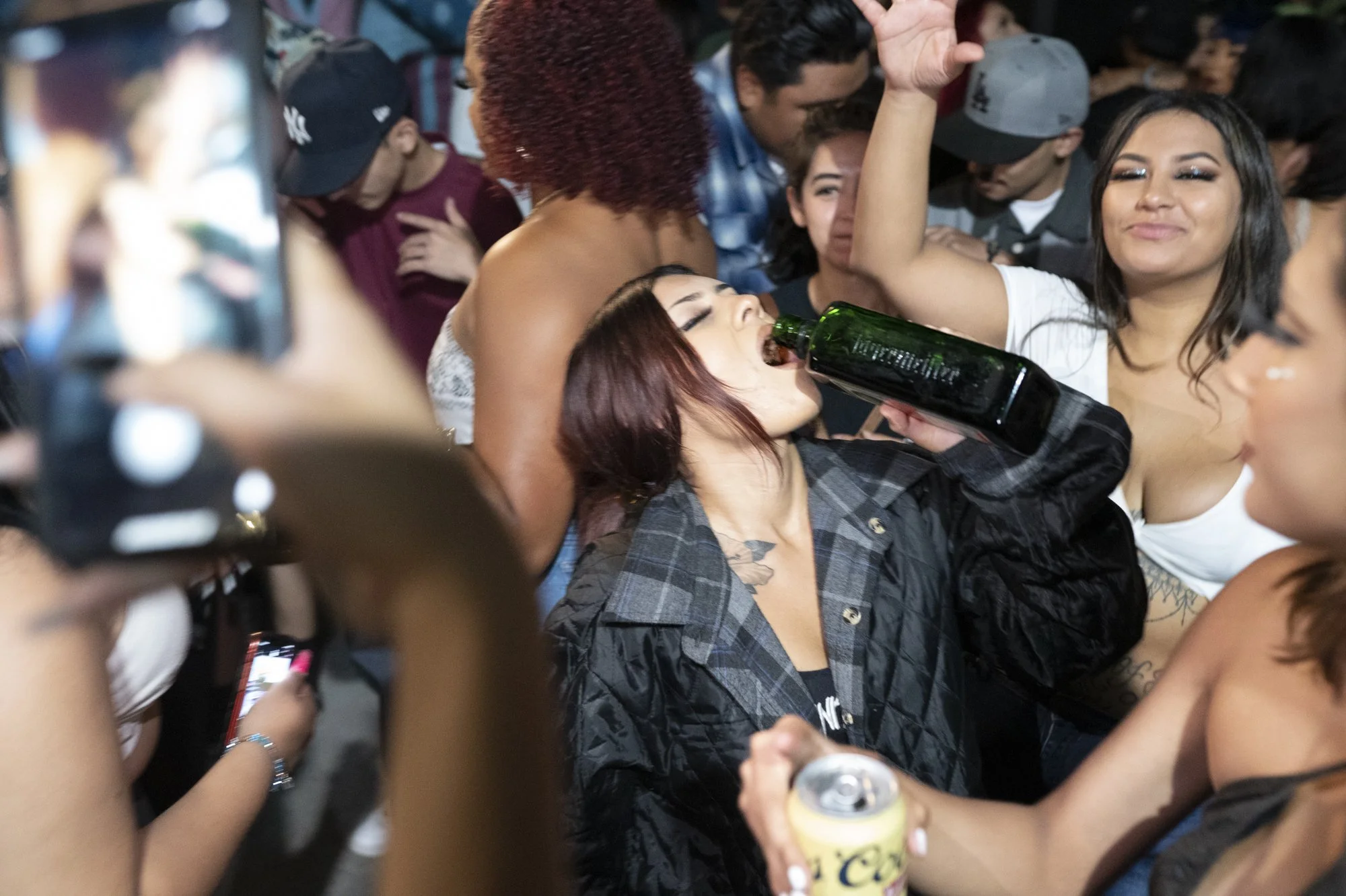 Close-up of a woman drinking from a bottle in a dense nighttime crowd at a Long Beach street gathering