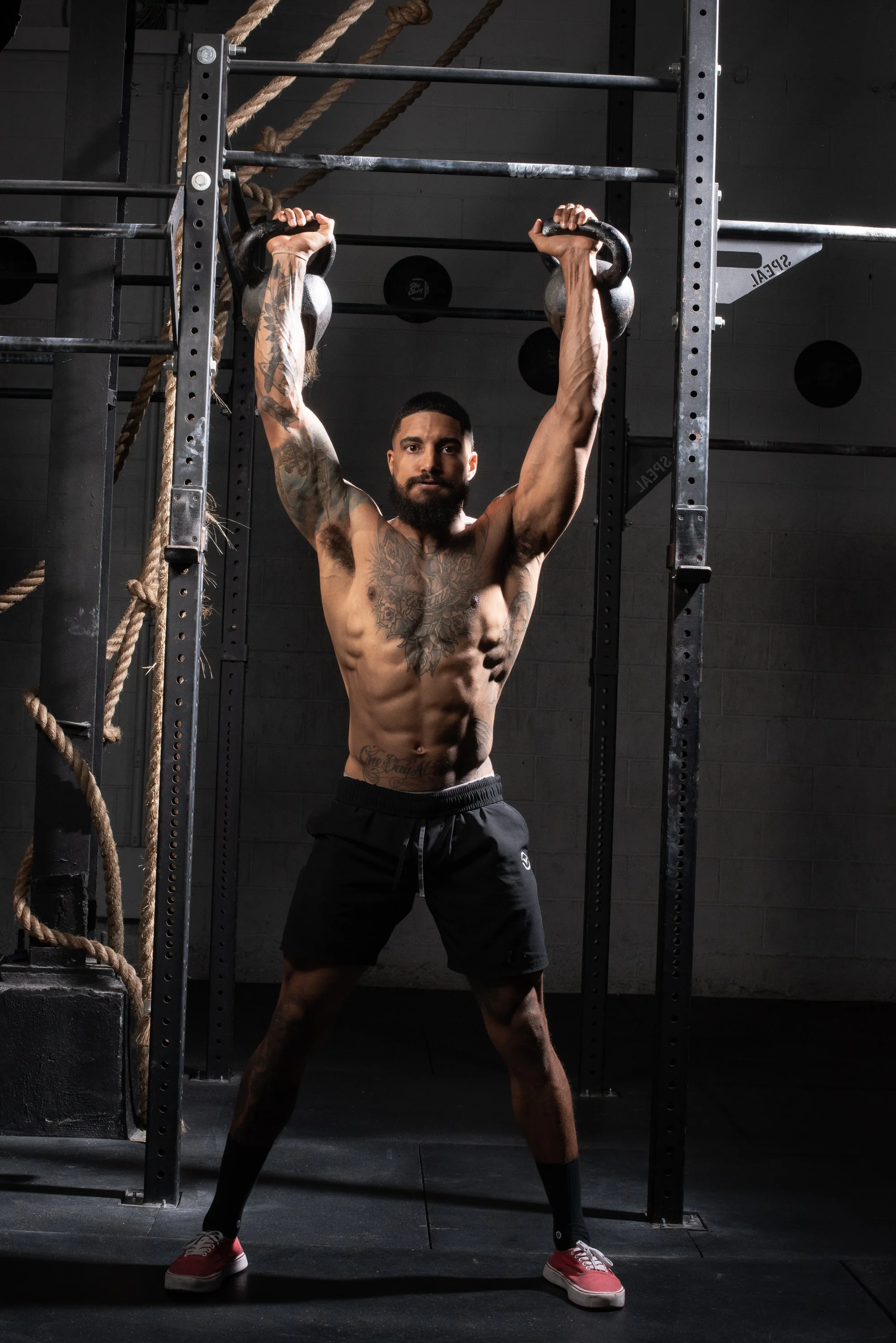 Athlete presses kettlebells overhead in a Colorado gym while standing inside a rack