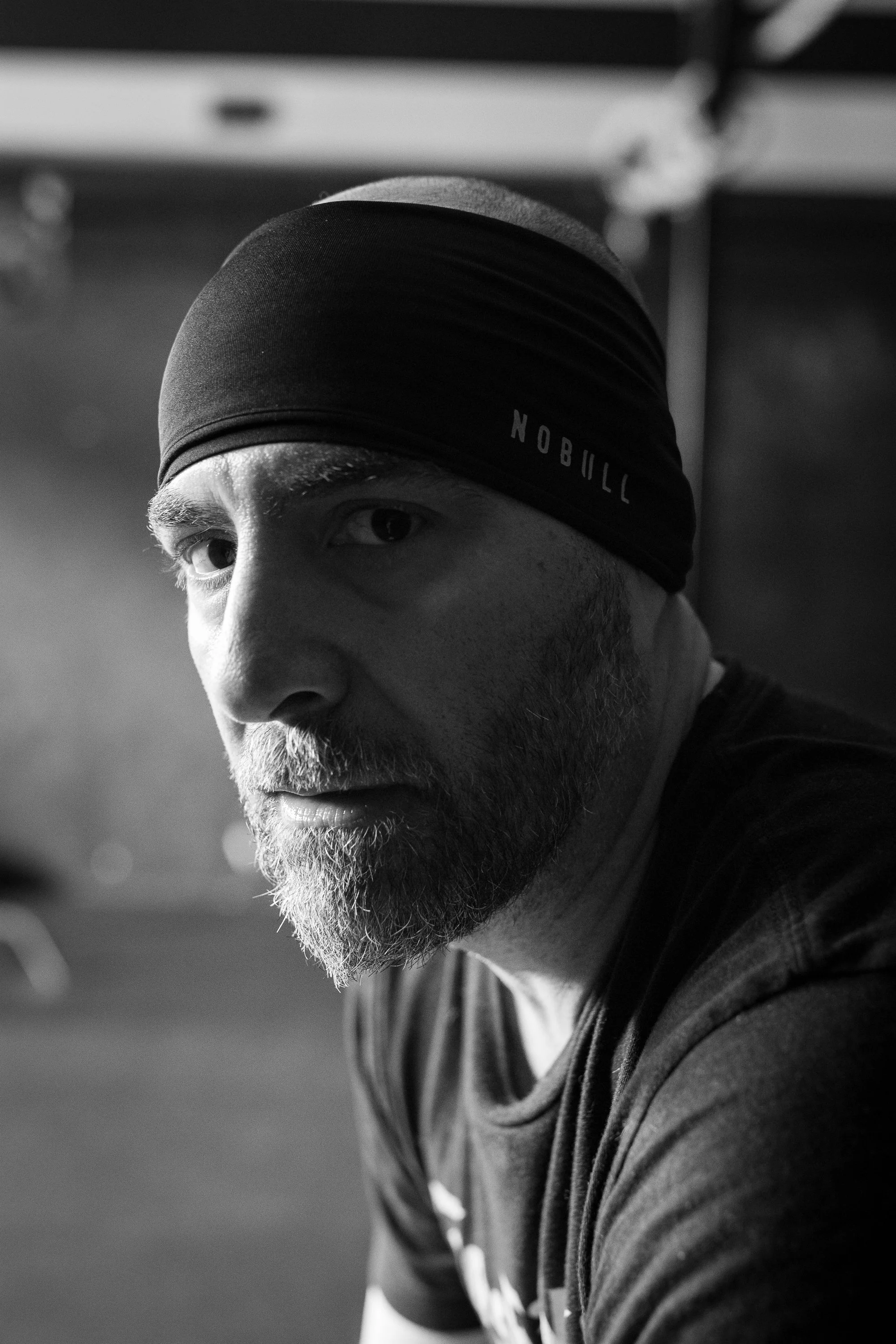 black and white fitness portrait of male athlete resting in gym wearing headband