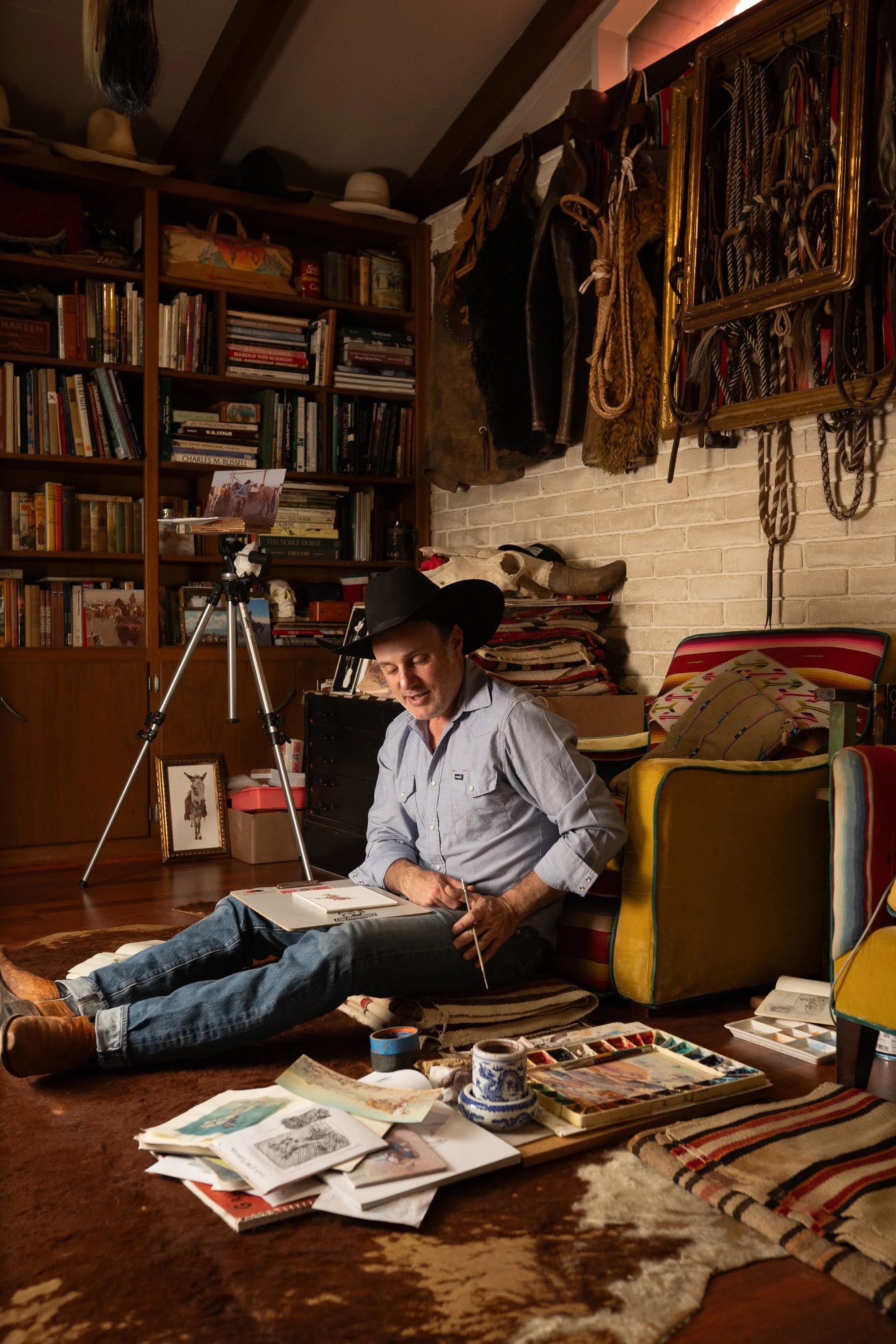 Teal Blake seated on studio floor surrounded by watercolor sketches and Western art materials