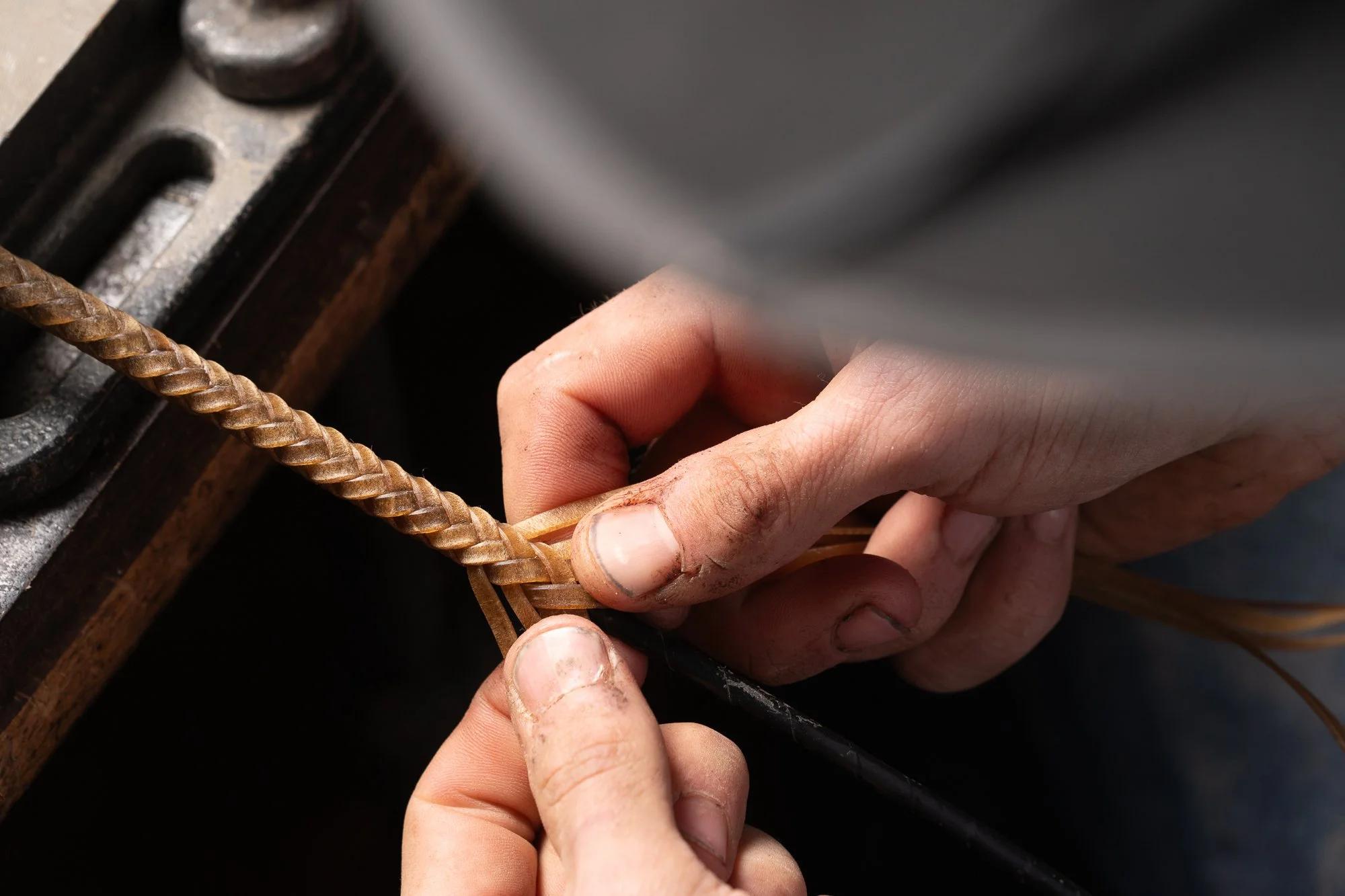 Close-up of hands weaving rawhide strands together to form a tight, even braid for handmade cowboy gear