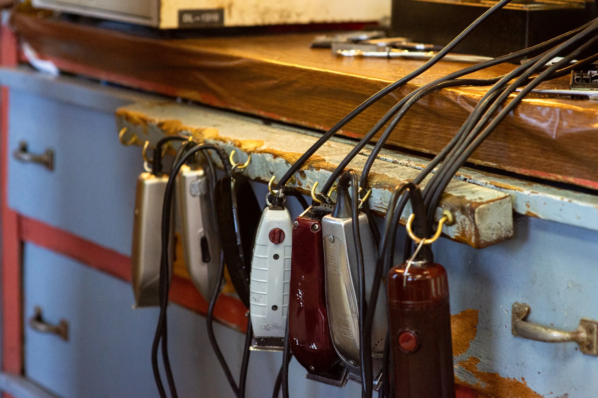 Close-up of barber clippers hanging from a worn workstation inside a barbershop