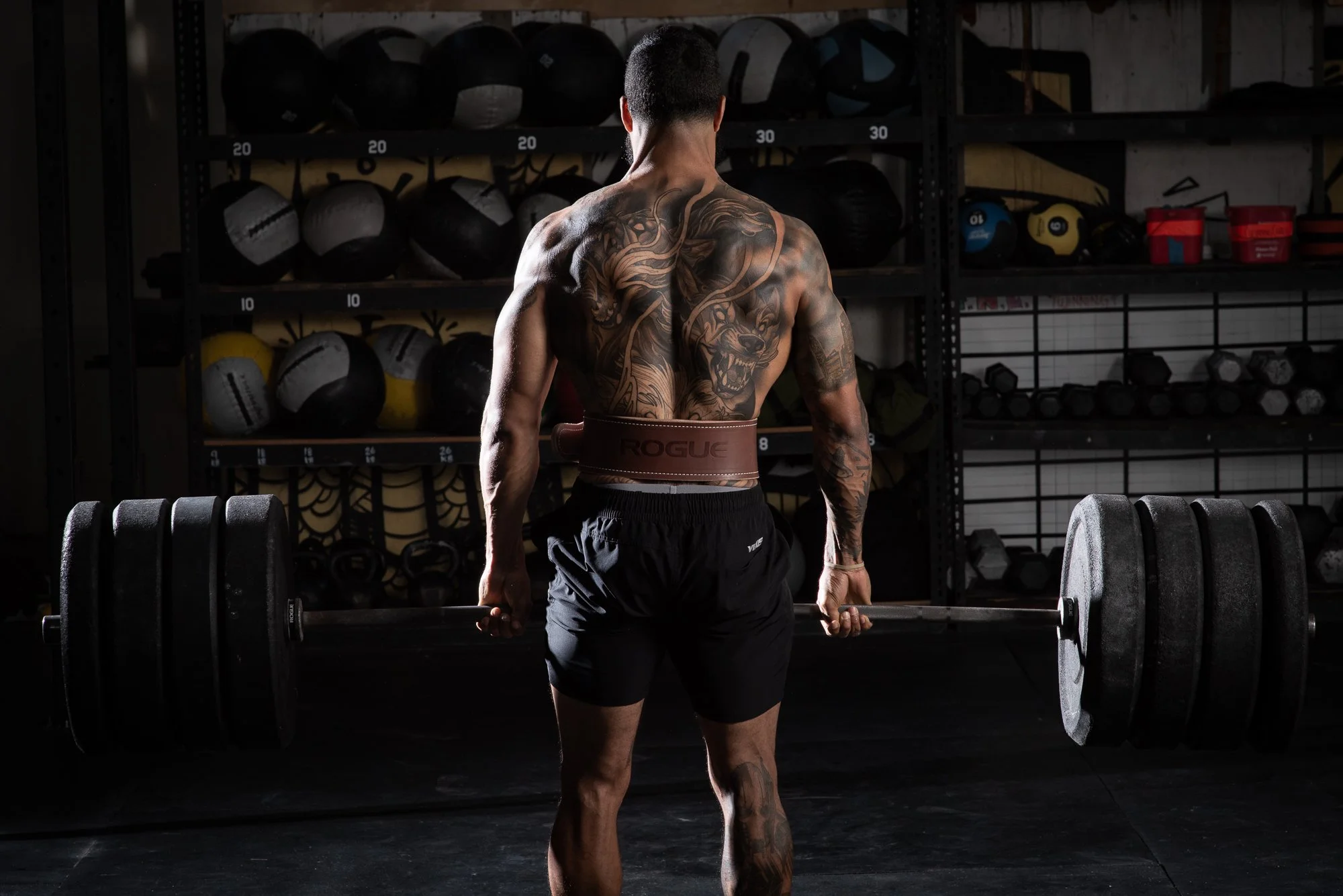 Athlete lifts a loaded barbell from the ground during a deadlift in a Colorado gym, viewed  from behind