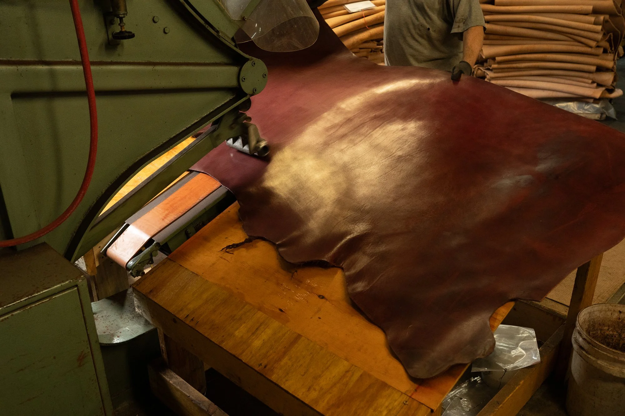 A broad brown leather hide feeds through a large metal processing machine as it is guided by hand