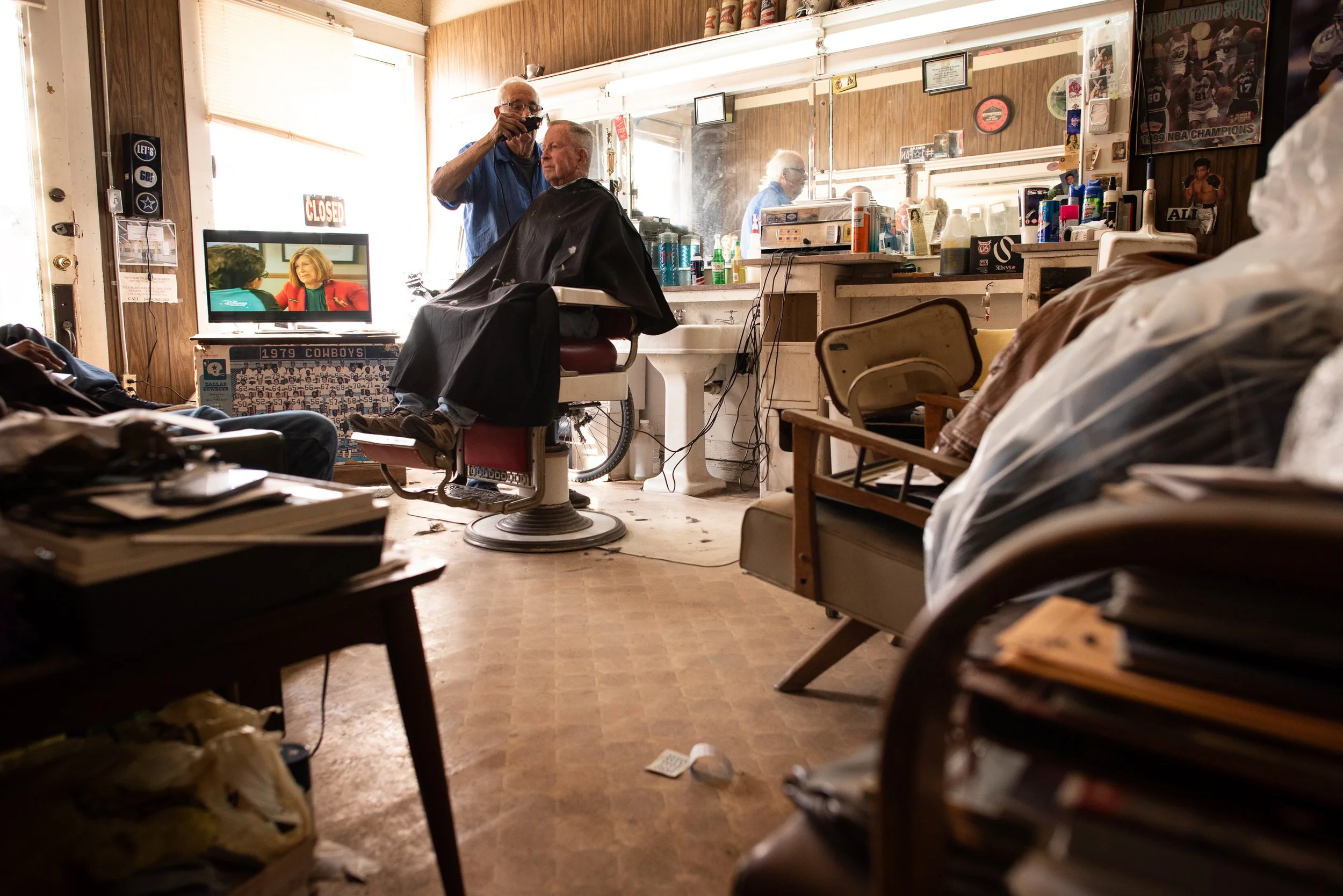 Elderly barber cutting a client’s hair inside a small barbershop in Marfa, Texas shortly before the shop closed.