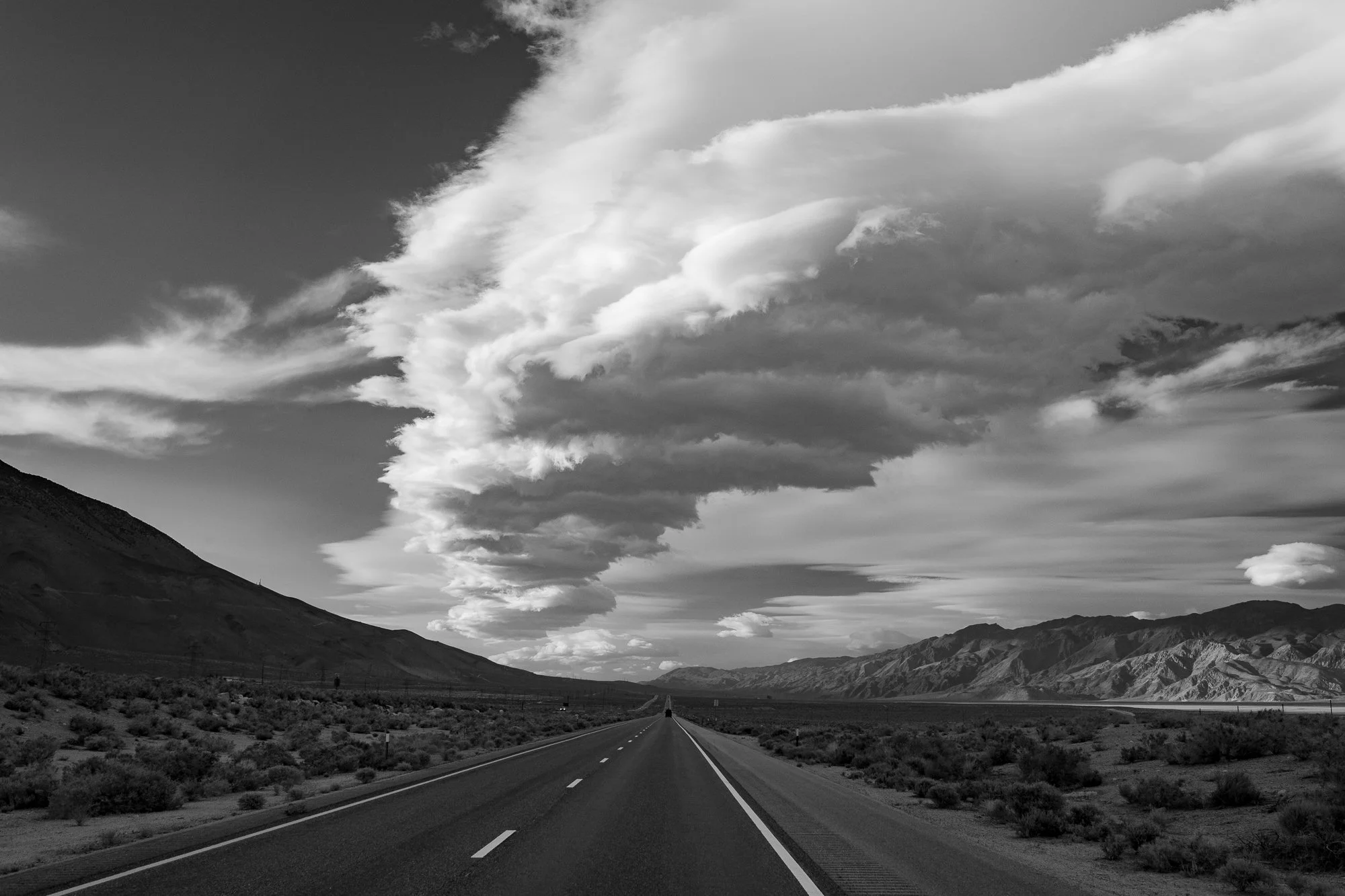 Black and white California desert highway with mountains and large clouds overhead