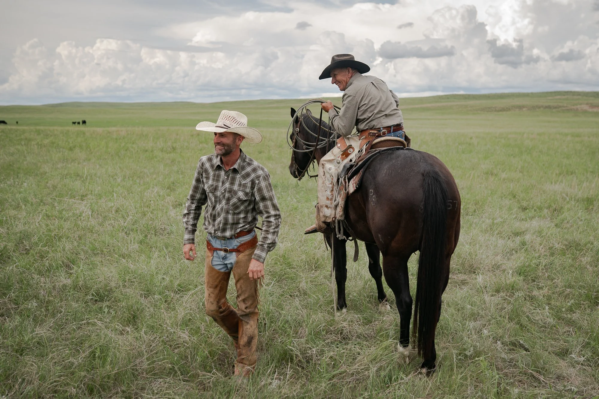 Cowboys walking and riding horses across grassy plains under cloudy sky