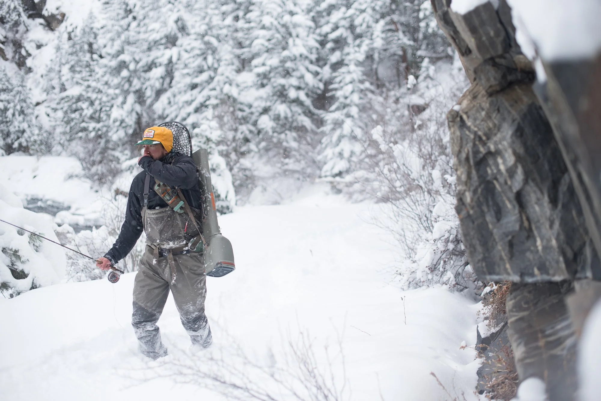 A fisherman walks along the snowy bank of Clear Creek carrying fishing gear in winter conditions.