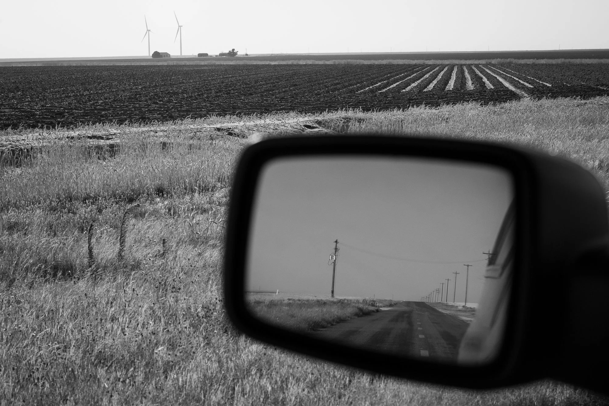 Black and white photograph of farmland reflected in a car mirror on the Llano Estacado
