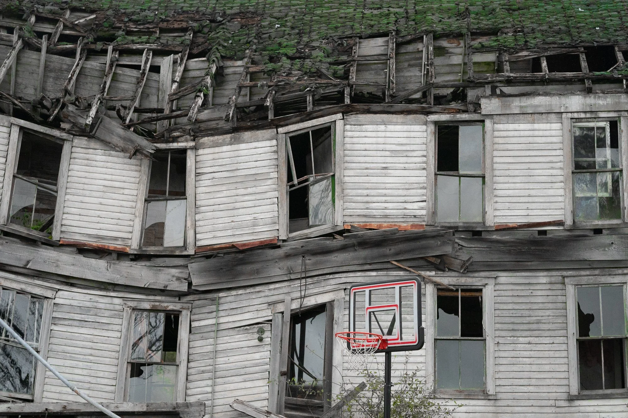 Photograph of a basketball hoop in front of an old dilapidated  house in Upstate New York