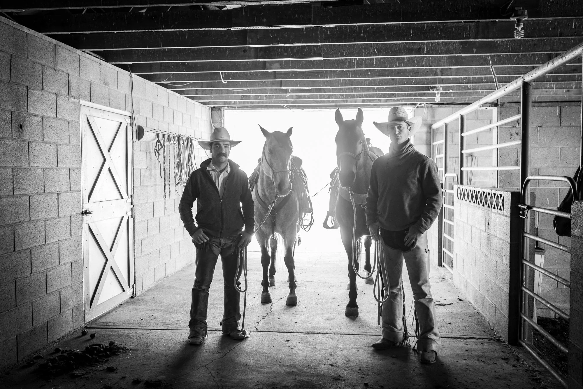 Two pen riders stand beside their horses inside the barn at Magnum Feedyard in Colorado