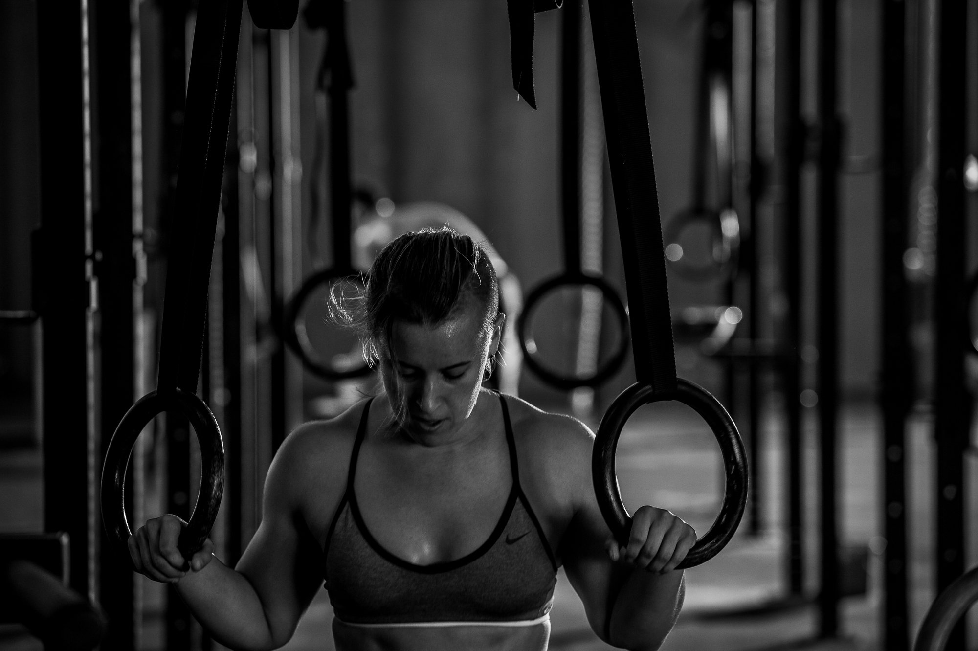 Female CrossFit athlete using gymnastic rings during a workout inside a gritty gym.