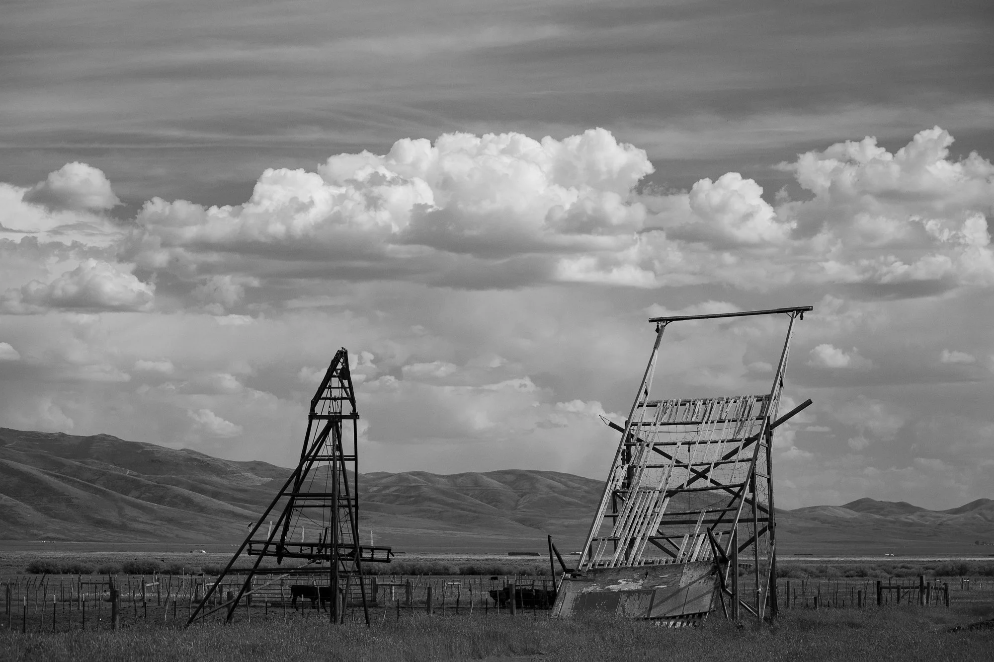 Black-and-white photograph of weathered cattle-handling equipment and fenced corrals on an open ranch beneath a cloudy sky.
