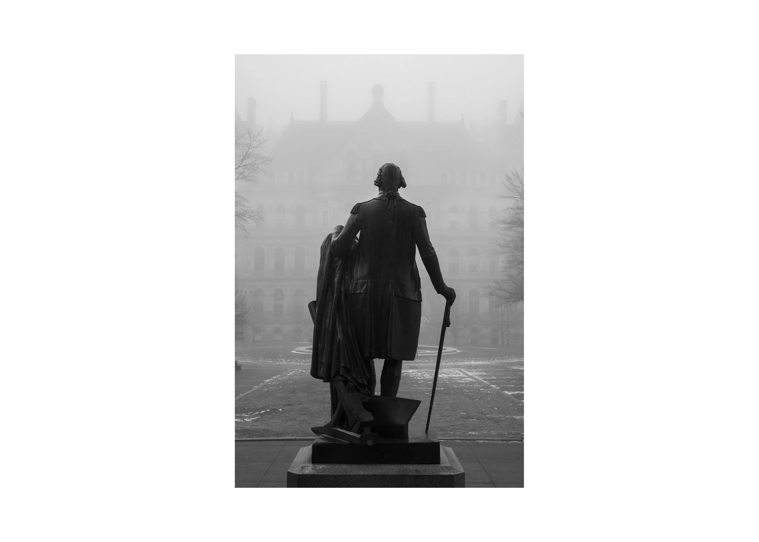 Black and white photograph of the George Washington statue in Albany, New York, viewed from behind with the New York State Capitol fading into winter fog