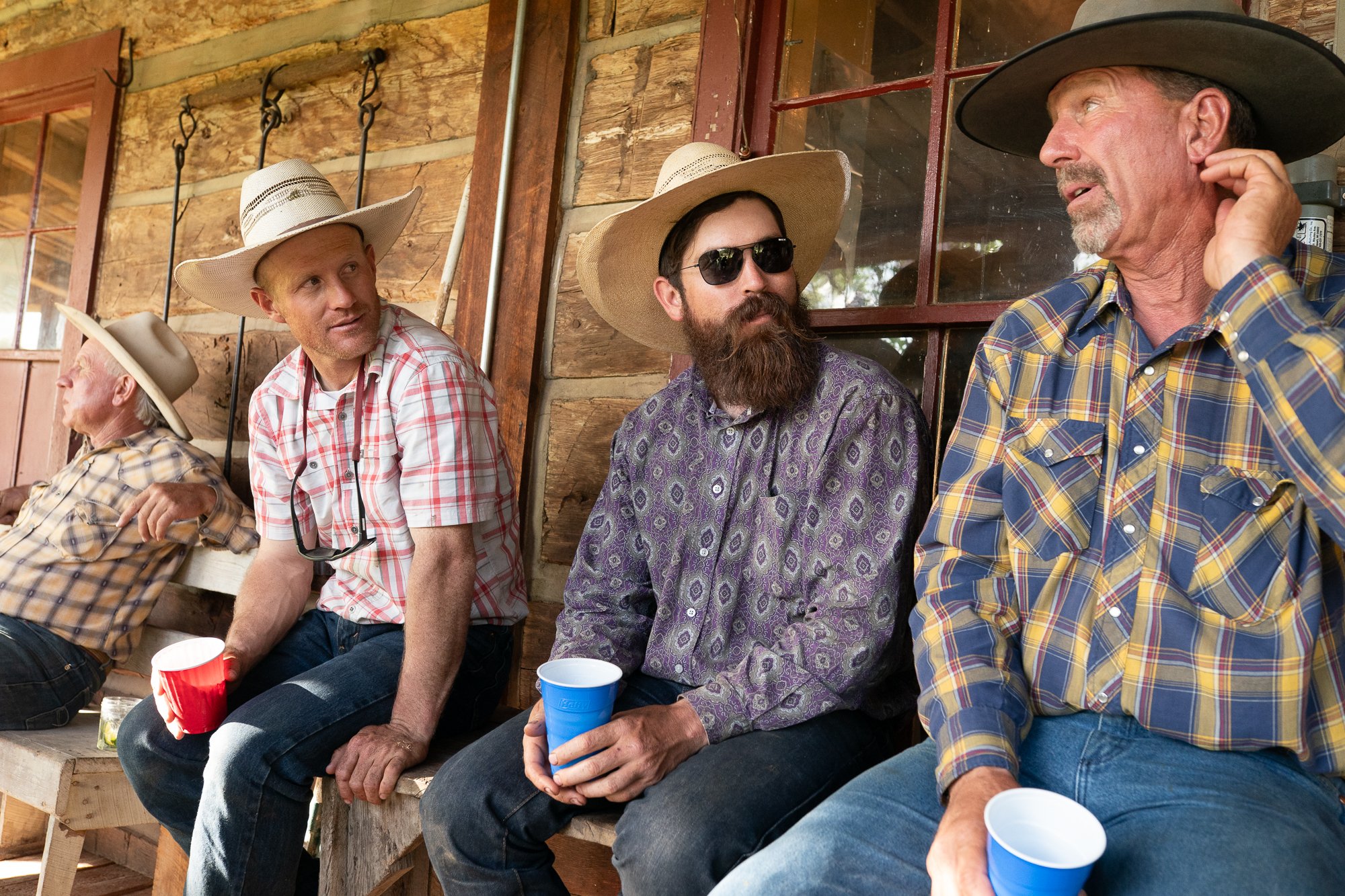 Group of cowboys sitting on rustic porch drinking and talking in casual setting