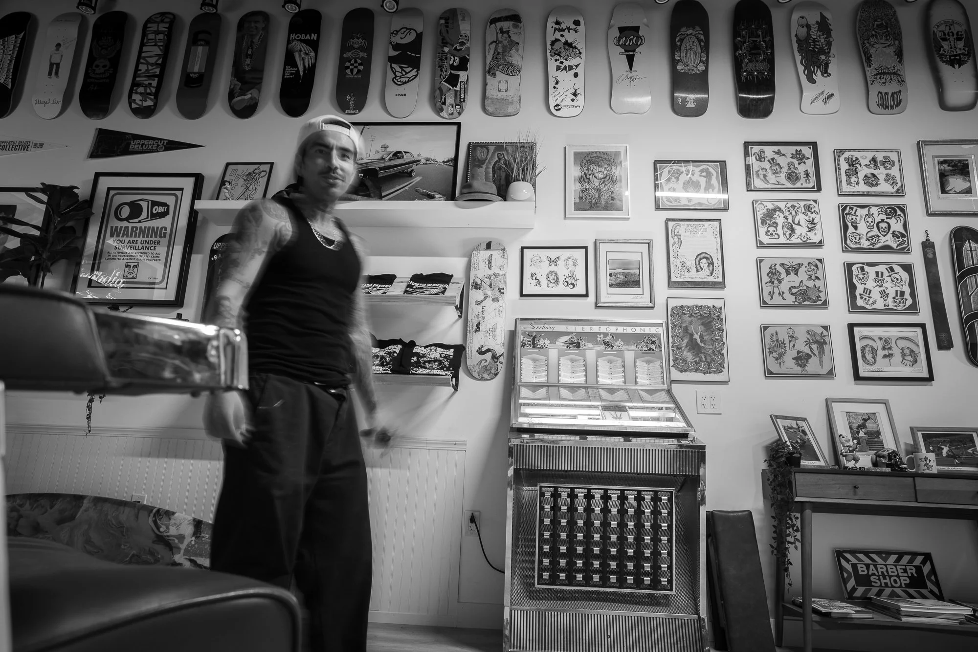 Emiliano Zermeno inside Leucadia Barbershop in Encinitas, California with skateboards displayed on the wall.
