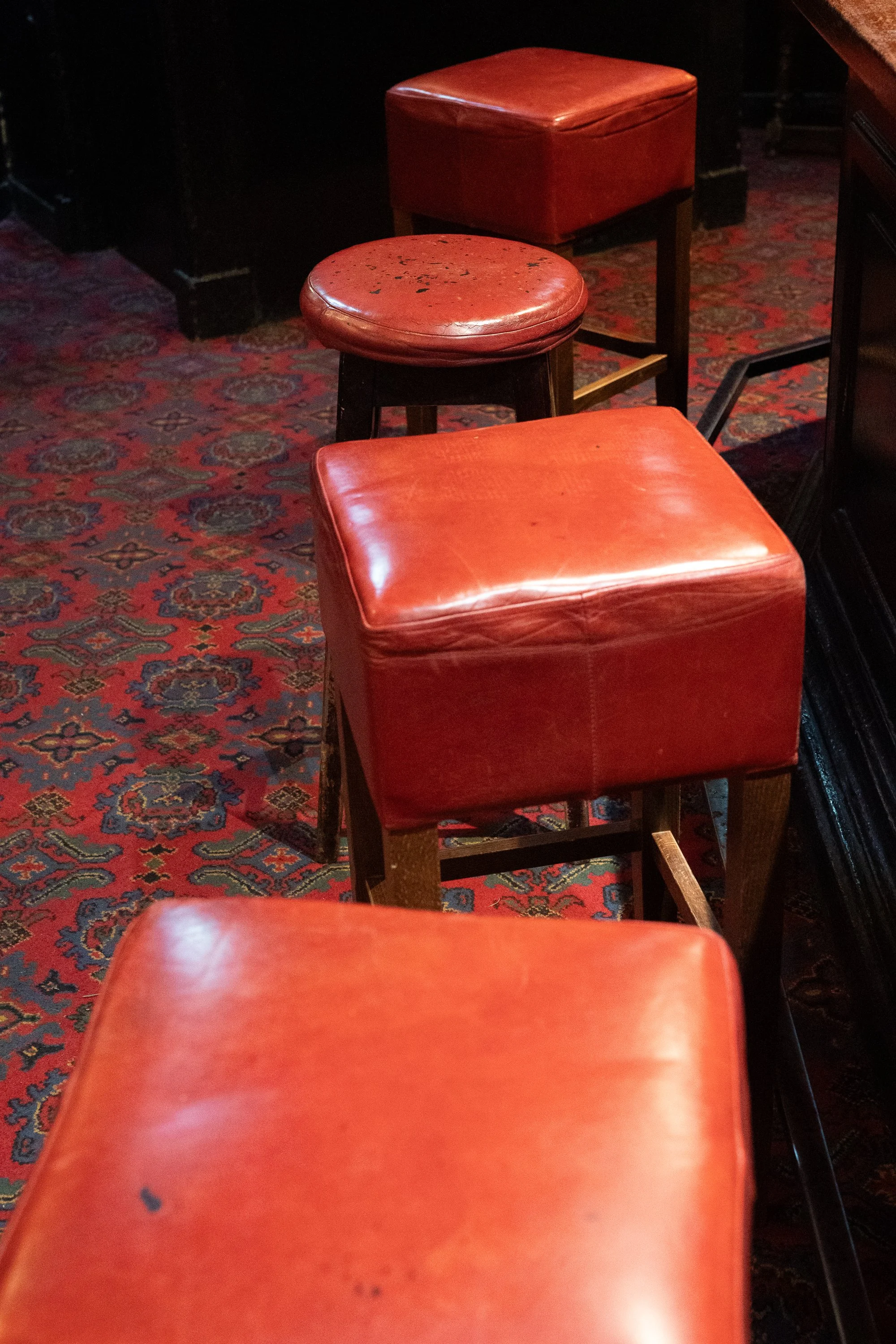 Red leather bar stools lined up on patterned carpet inside a traditional Edinburgh pub