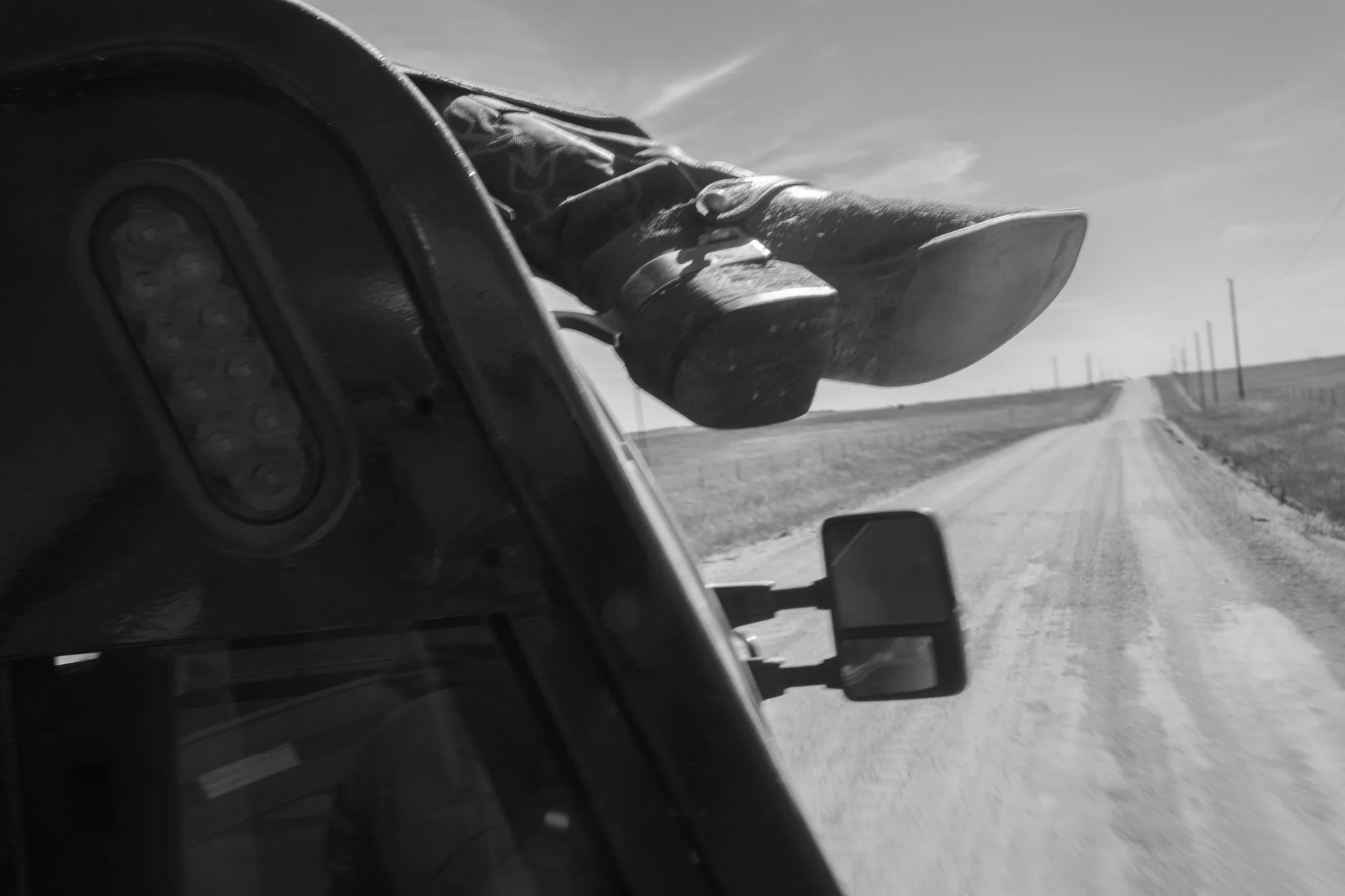 A cowboy's boots hang from the side of a ranch truck traveling a gravel road at Silver Spur Ranch