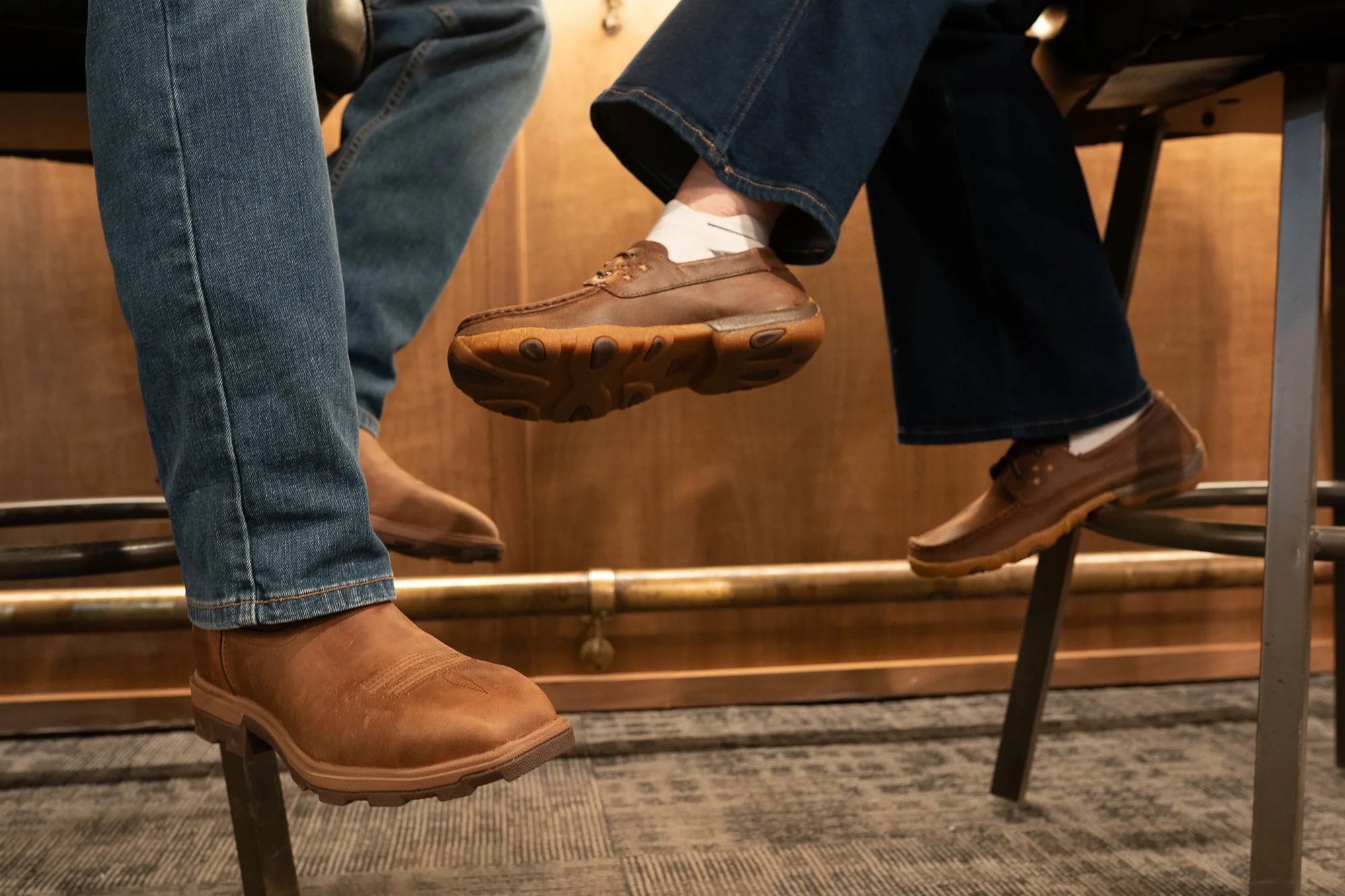 Close detail of boots and shoes worn by people seated at a bar inside a VFW hall