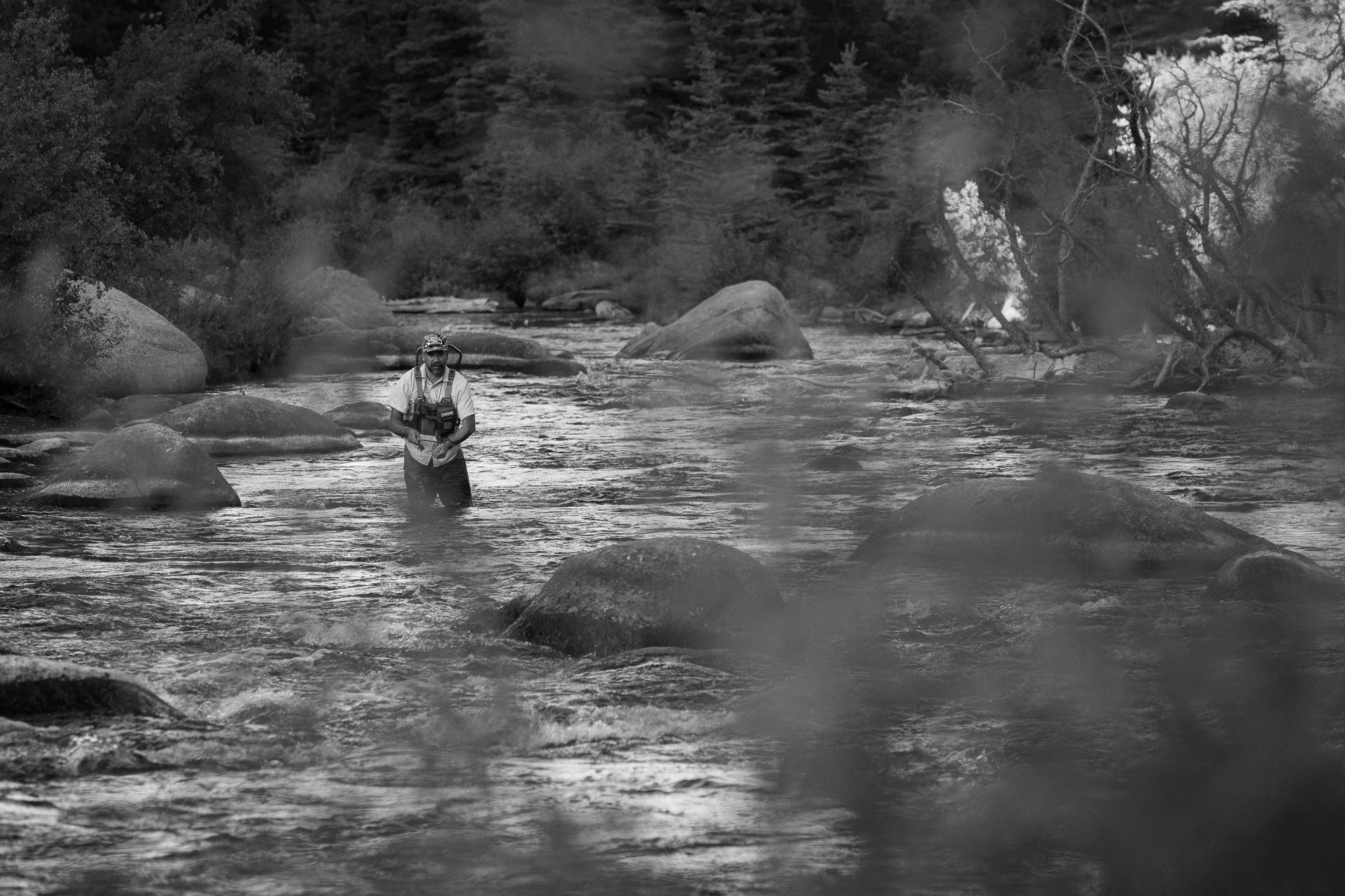A fly fisherman wades through the South Platte River in 11 Mile Canyon, Colorado, surrounded by smooth granite boulders.