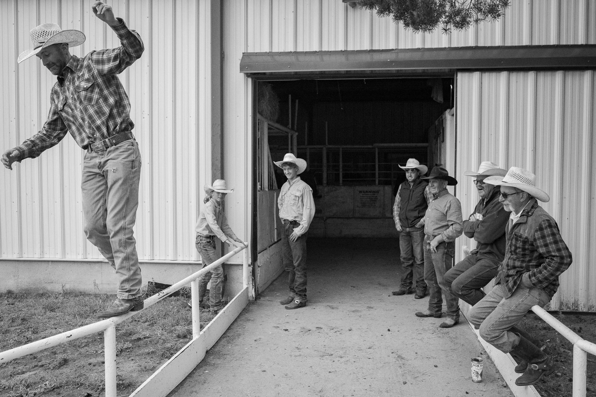 Cowboys watch as their friend tries to walk along a railing without falling off