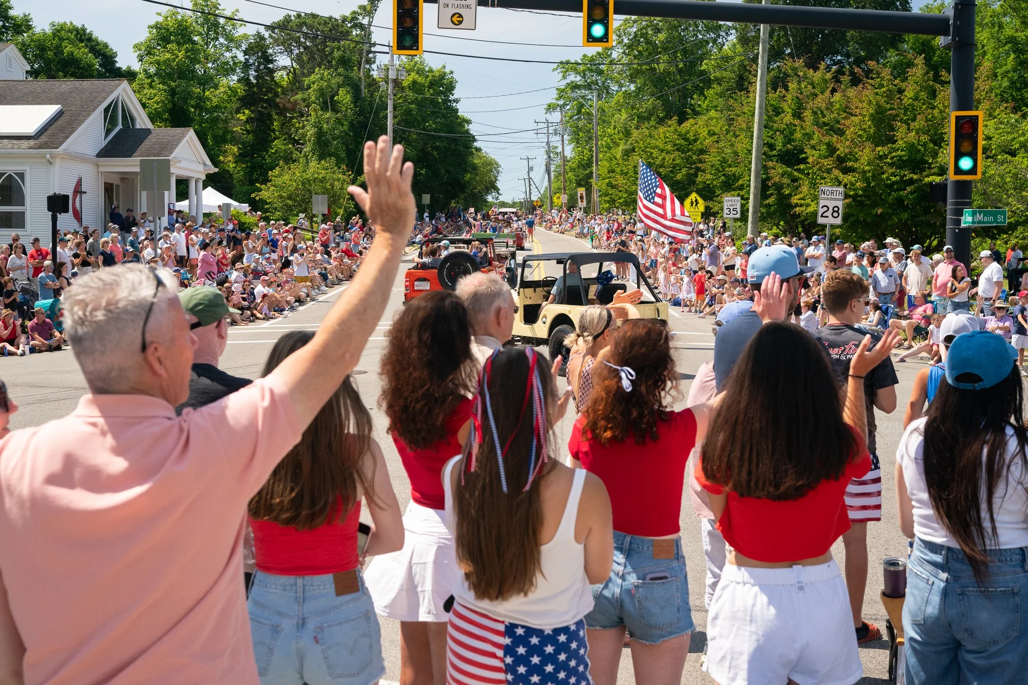 Crowd gathered along a Cape Cod road watching a 4th of July parade with American flags and summer atmosphere