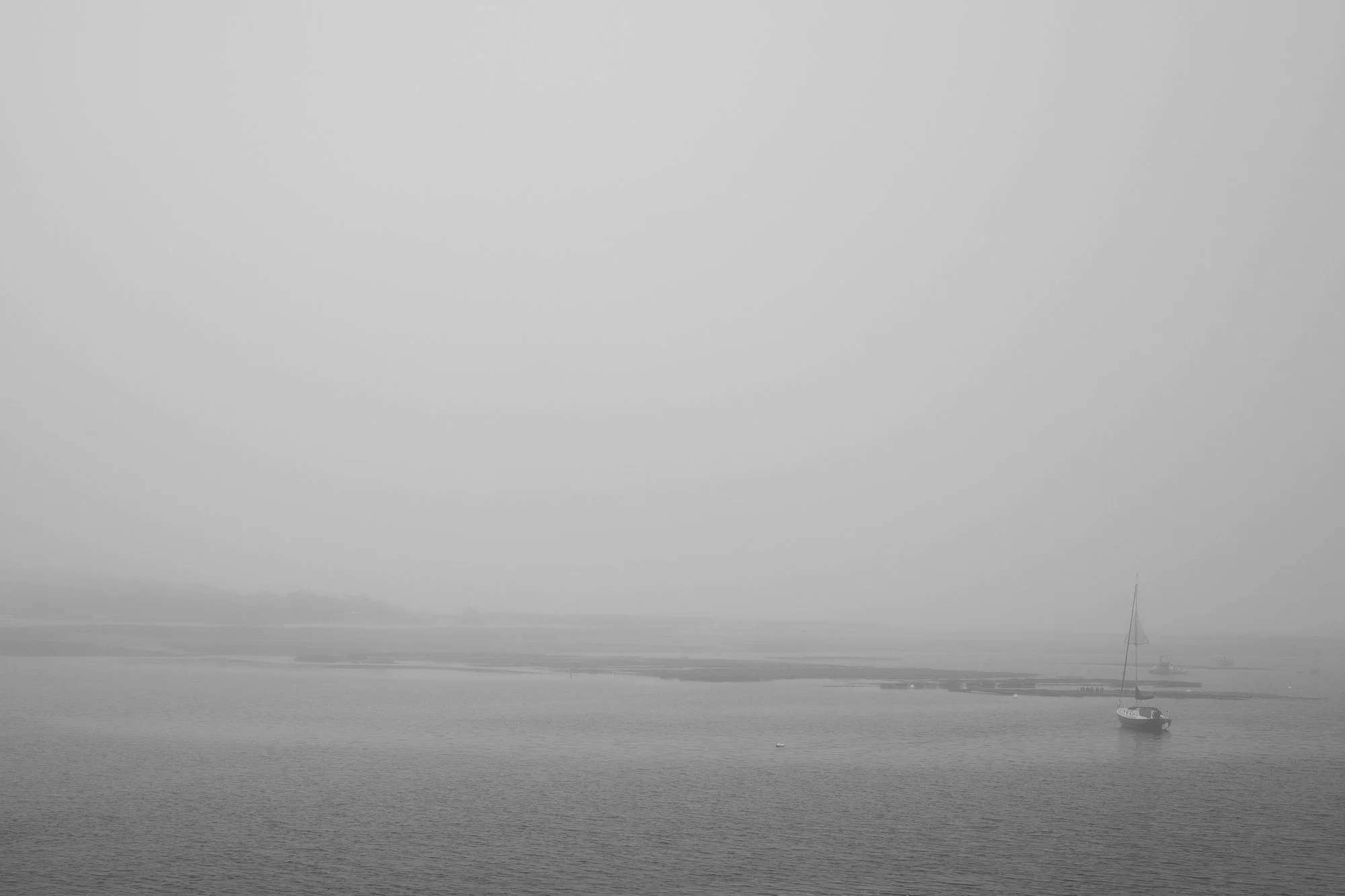 Foggy scene at Wellfleet Harbor on Cape Cod with a sailboat anchored in calm water