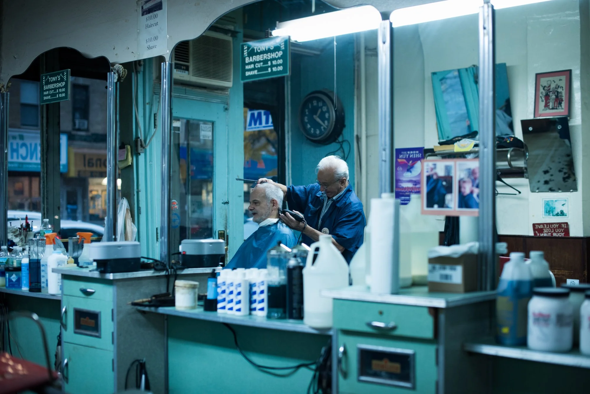 A barber trims a client’s hair as seen through mirrors inside Tony’s Barbershop in Brooklyn, New York.