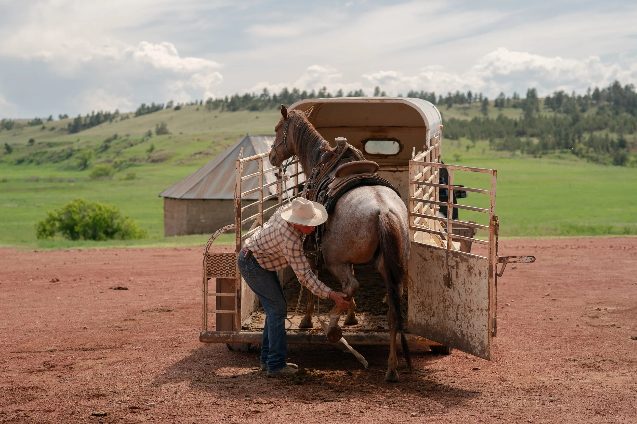 Buck Brannaman guiding a horse stepping into a trailer on a ranch in Montana