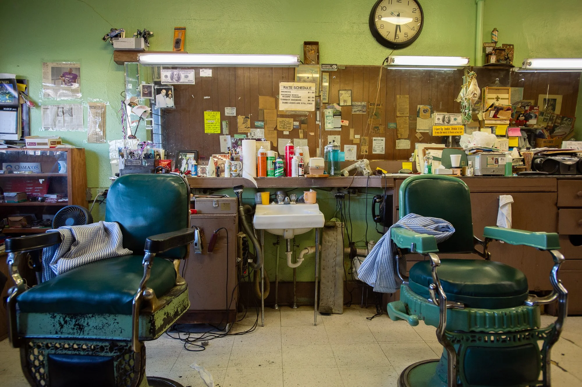 Two vintage green barber chairs facing a cluttered mirror and work station in a traditional shop