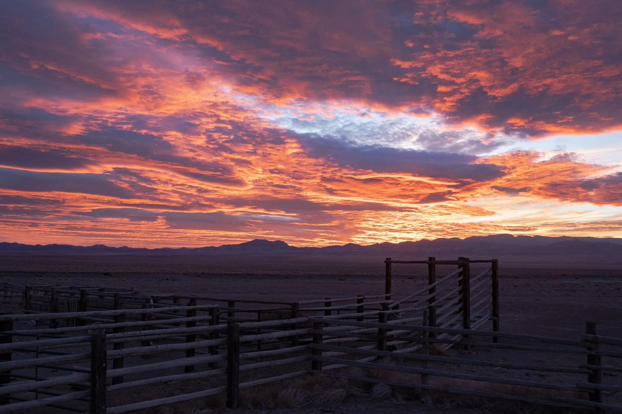 Sunset over empty cattle pens with dramatic sky and mountain horizon