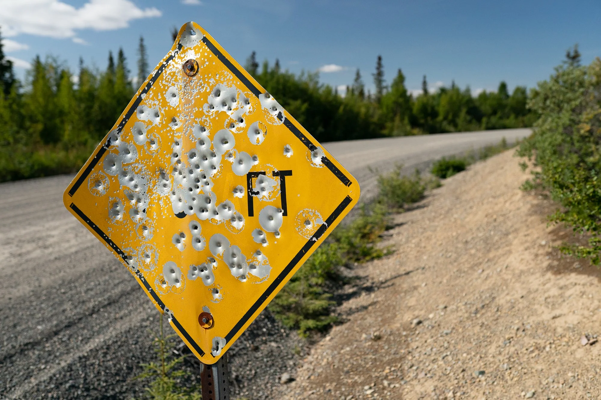 Weathered road sign beside a gravel road in Alaska