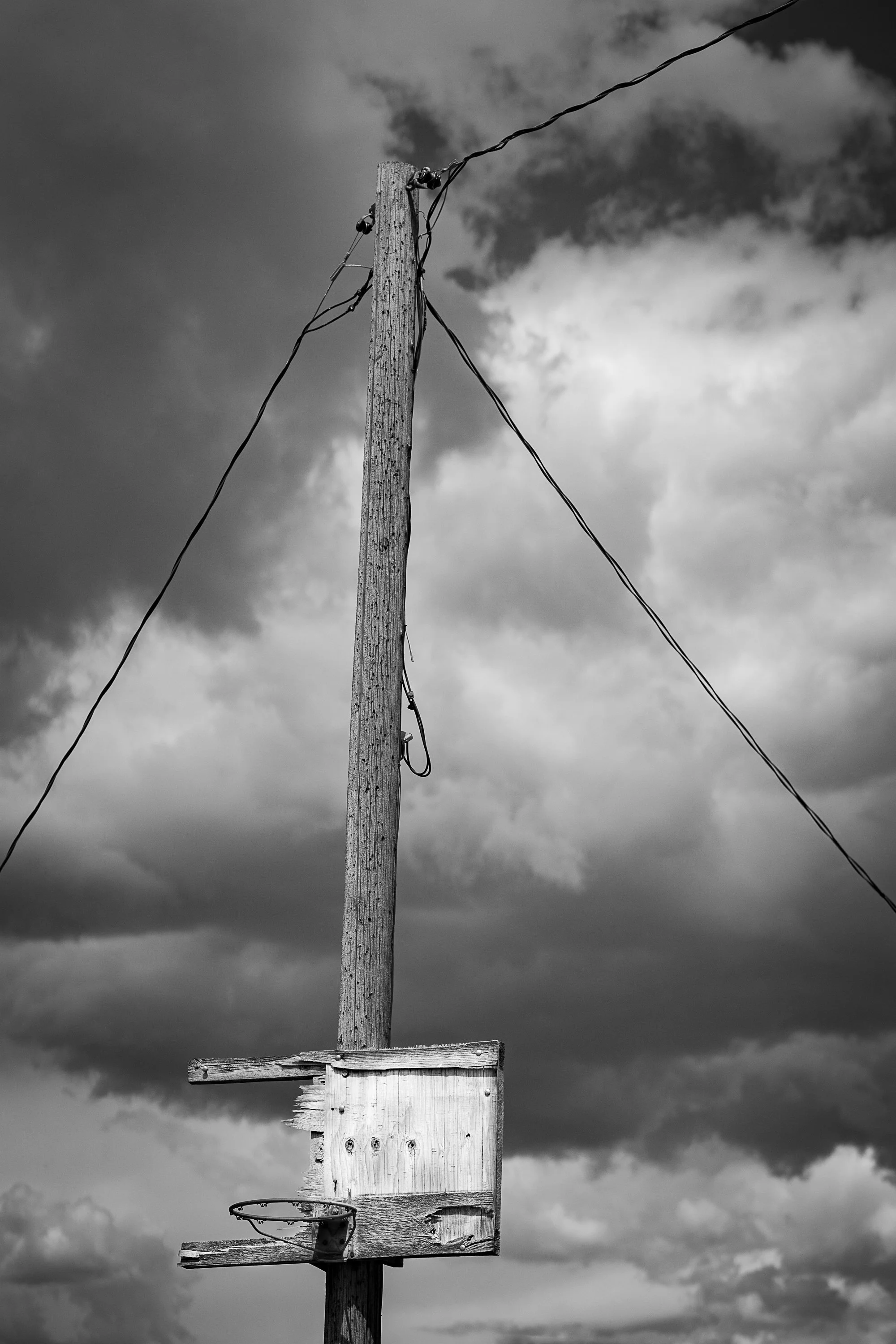 black and white photo of weathered wooden basketball hoop on pole under cloudy sky