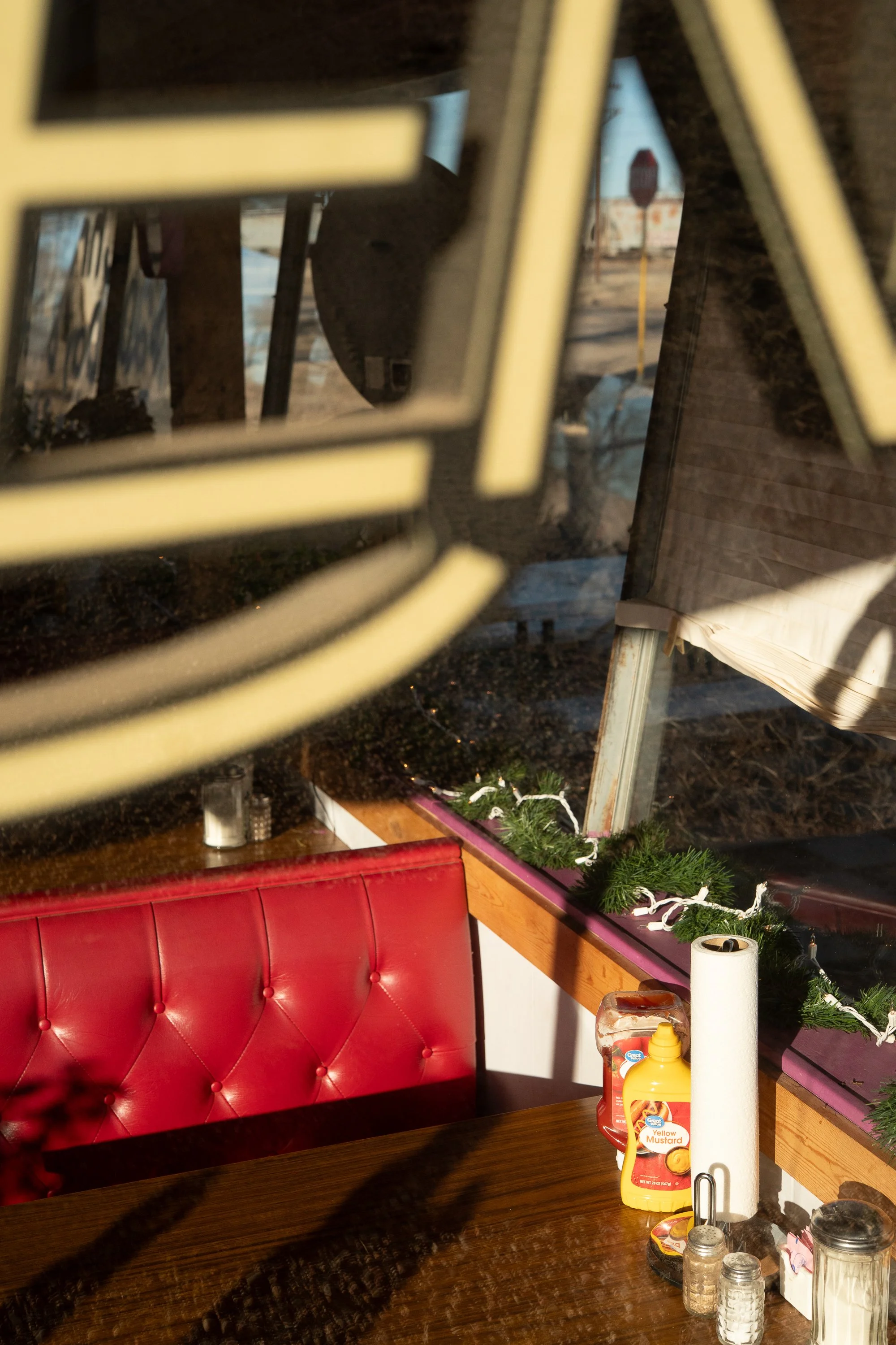 Red upholstered booth beside a diner window, with condiments, napkins, and shakers arranged on the table.