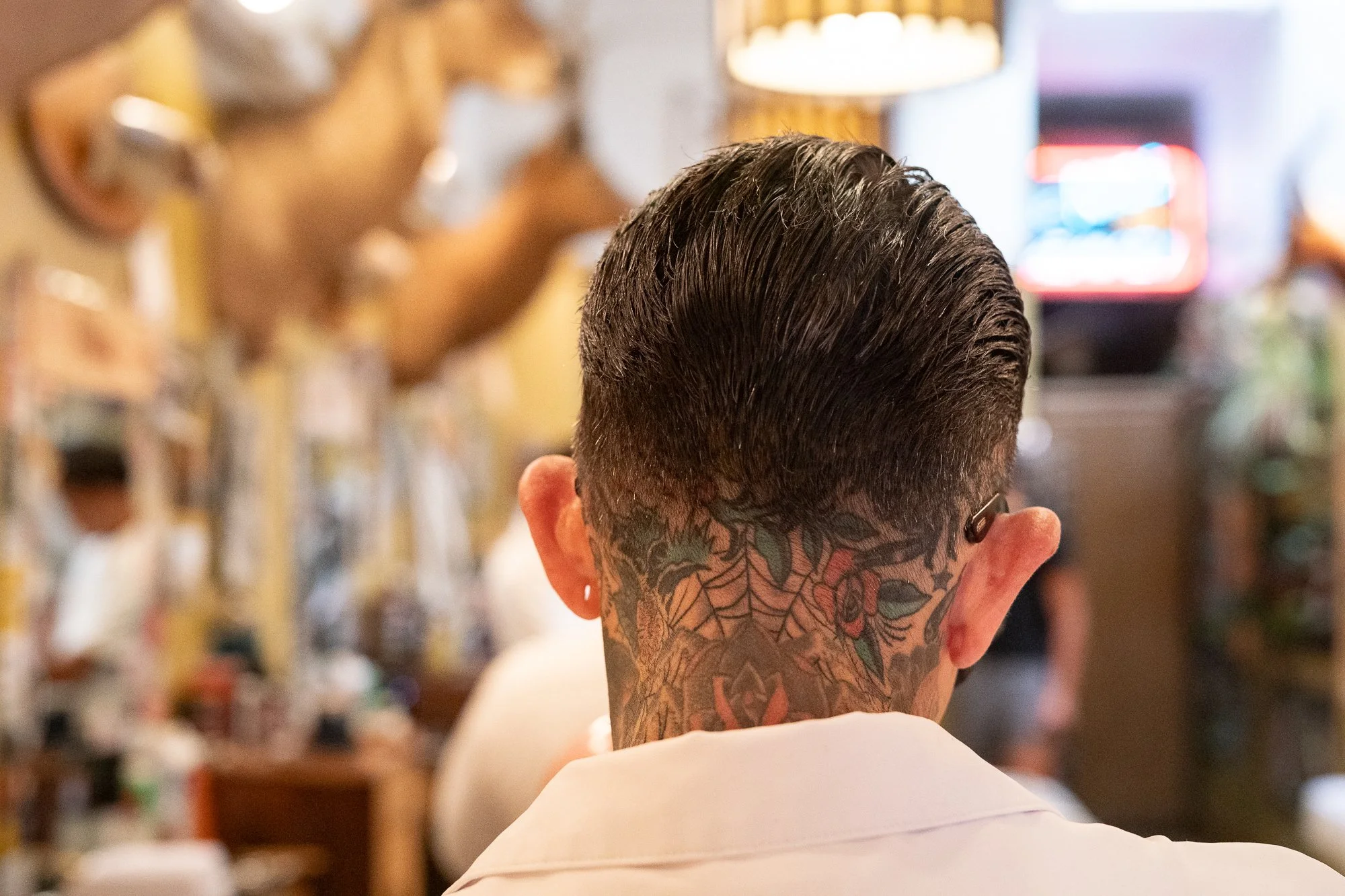 Close-up of a barber’s slicked-back haircut and neck tattoo as he works inside Pugsly’s SideShow Barbershop in Kingston, New York.