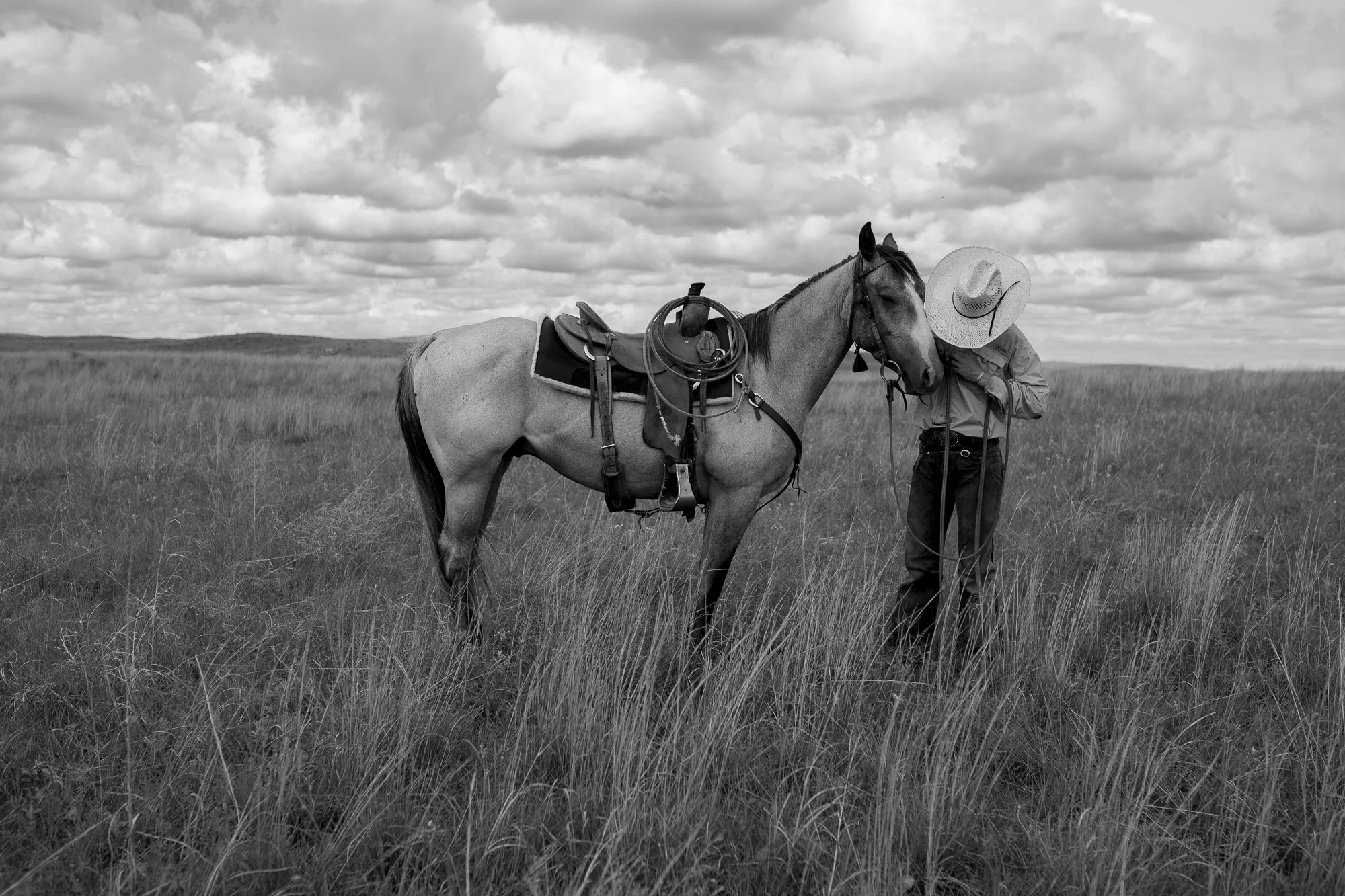 Cowboy standing beside a saddled horse in tall prairie grass at Haythorn Ranch in the Nebraska Sandhills.