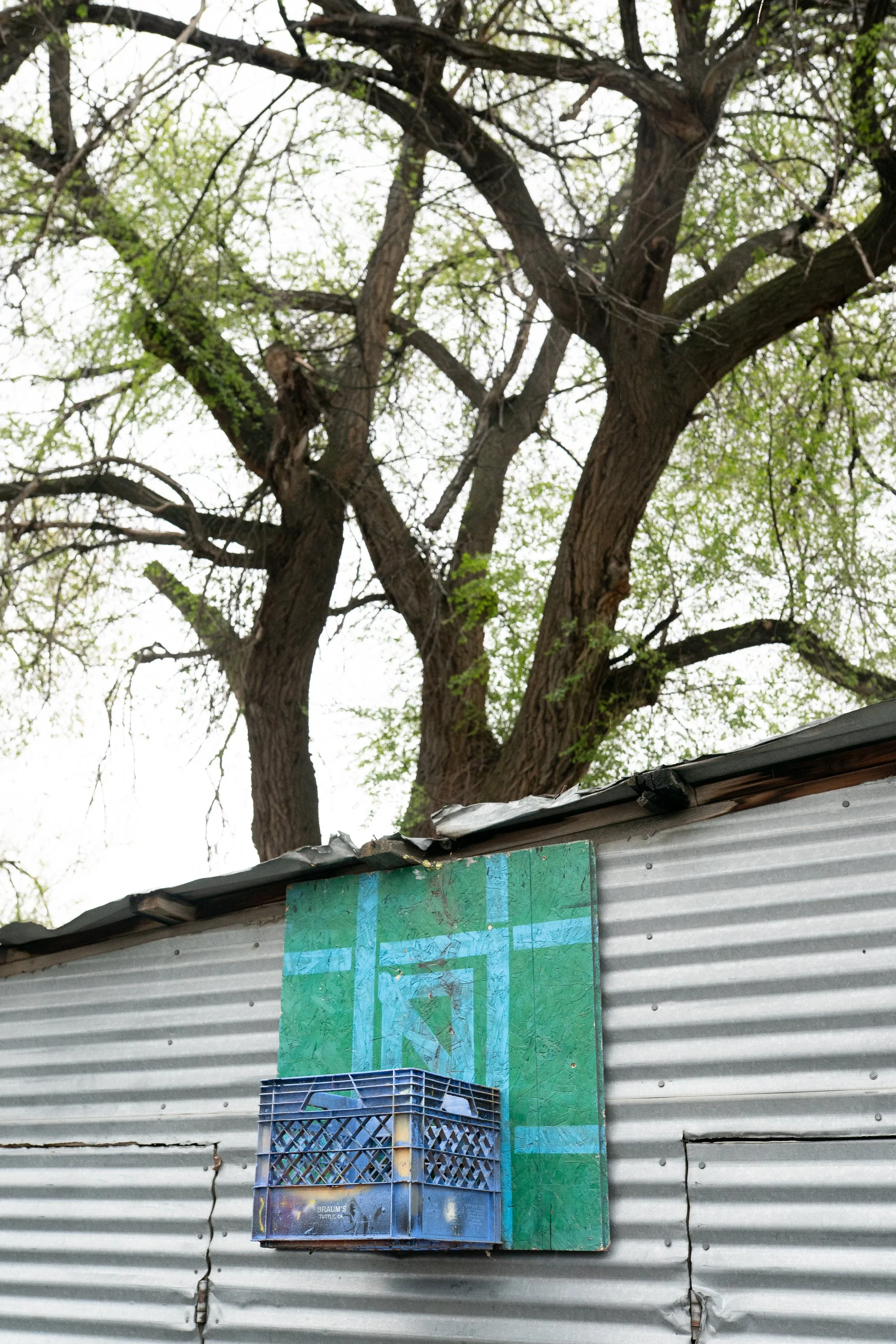 Makeshift basketball hoop with a crate rim and hand-painted backboard on a corrugated metal wall.