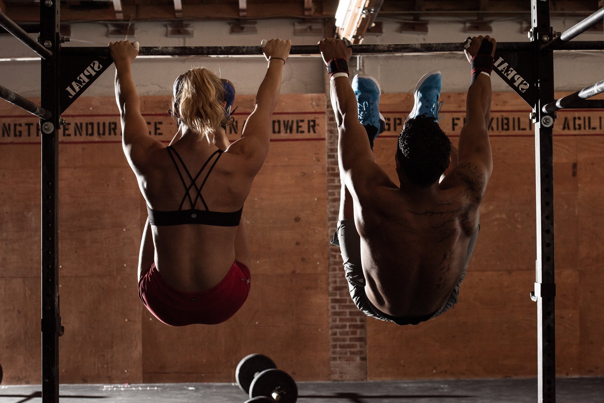 Two CrossFit athletes performing hanging leg raises on a pull-up rig in Boulder, Colorado.