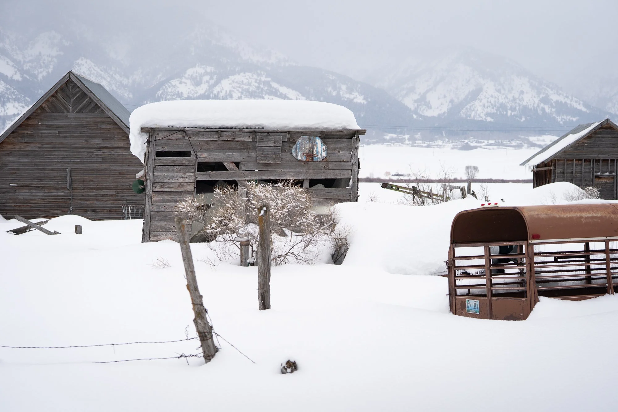 Snow covered ranch buildings and livestock trailer beneath Wyoming mountains