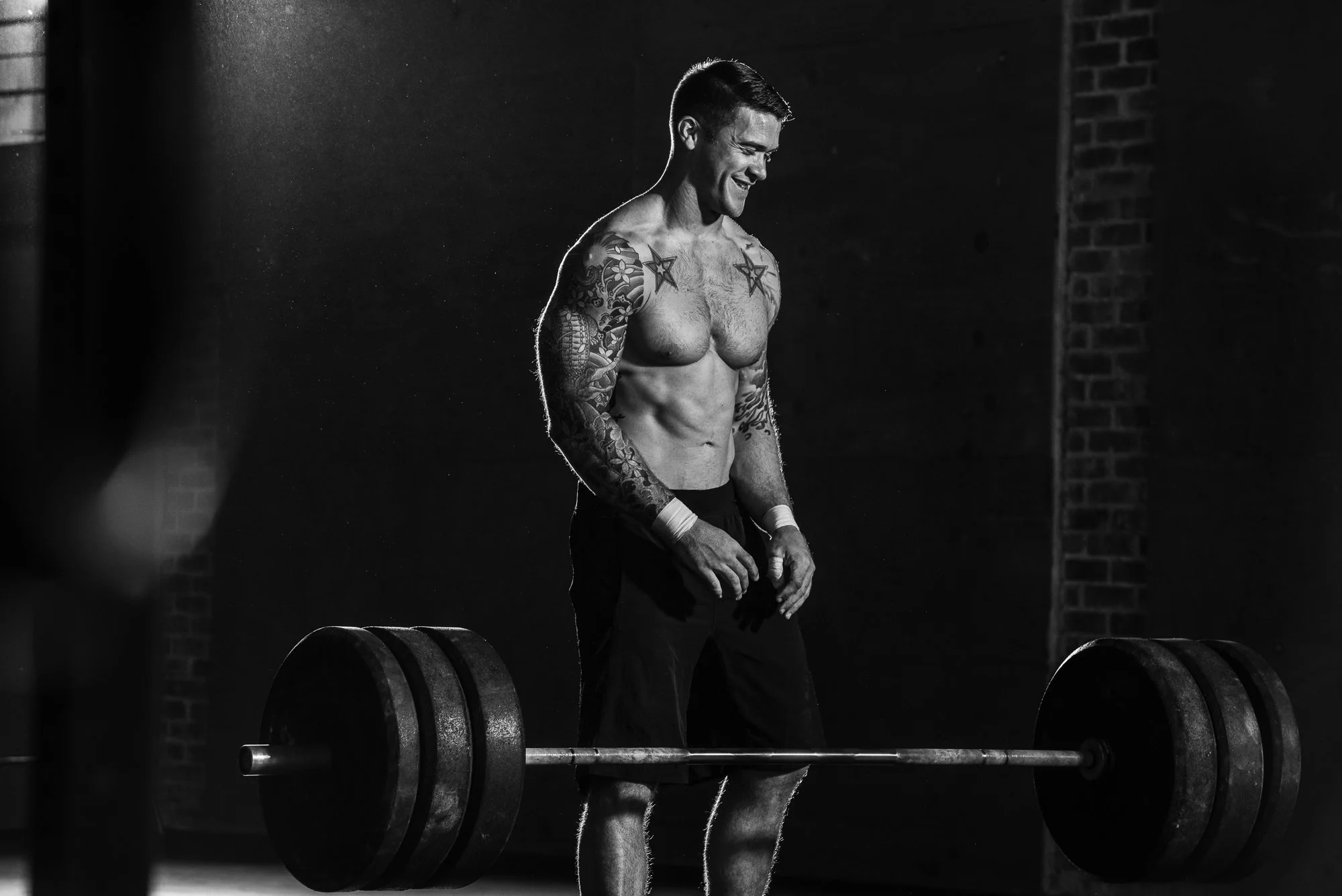 CrossFit athlete standing over a heavily loaded barbell during a workout in a gritty gym.