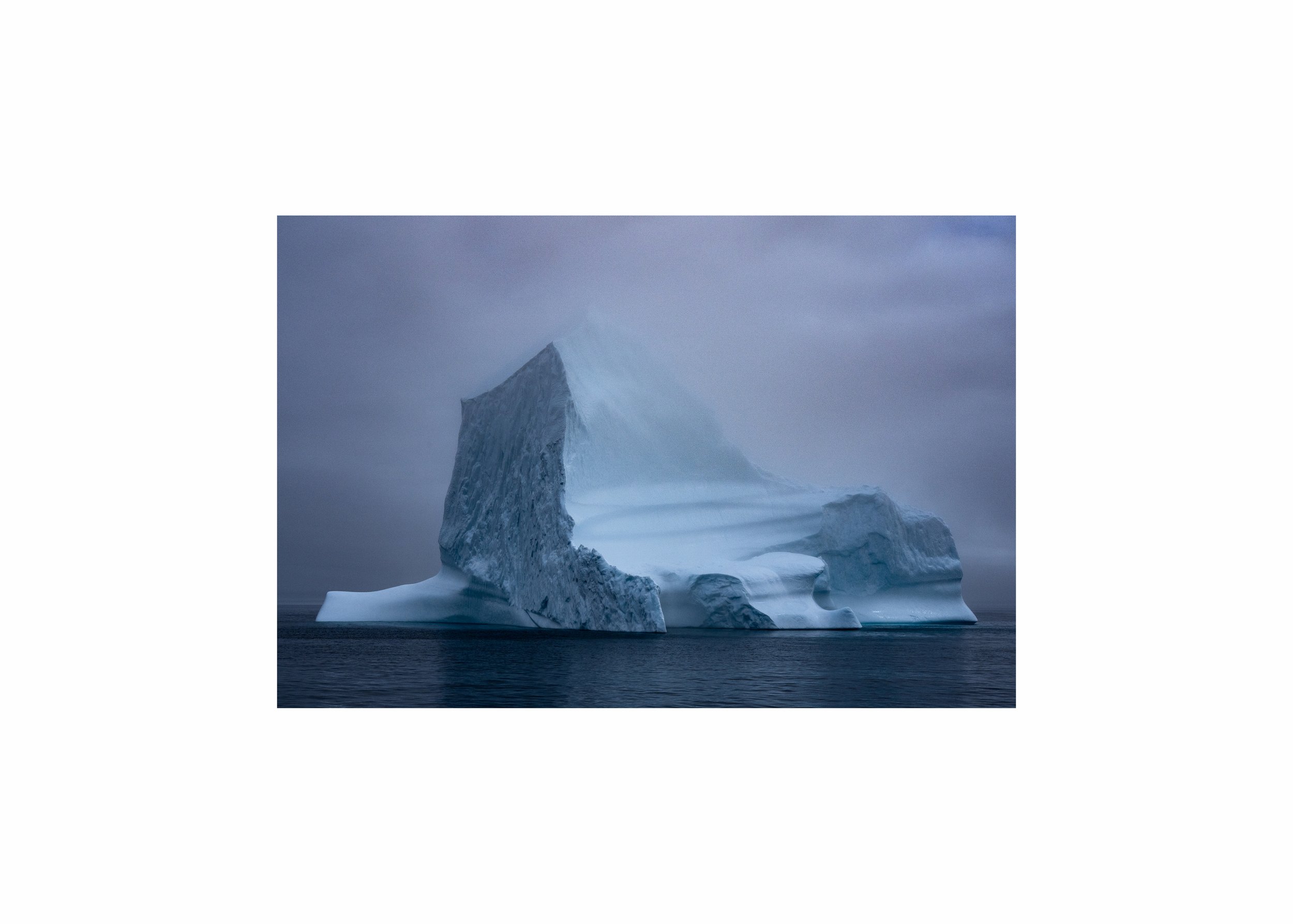 A massive, blue-toned sculpted iceberg in dark ocean water.