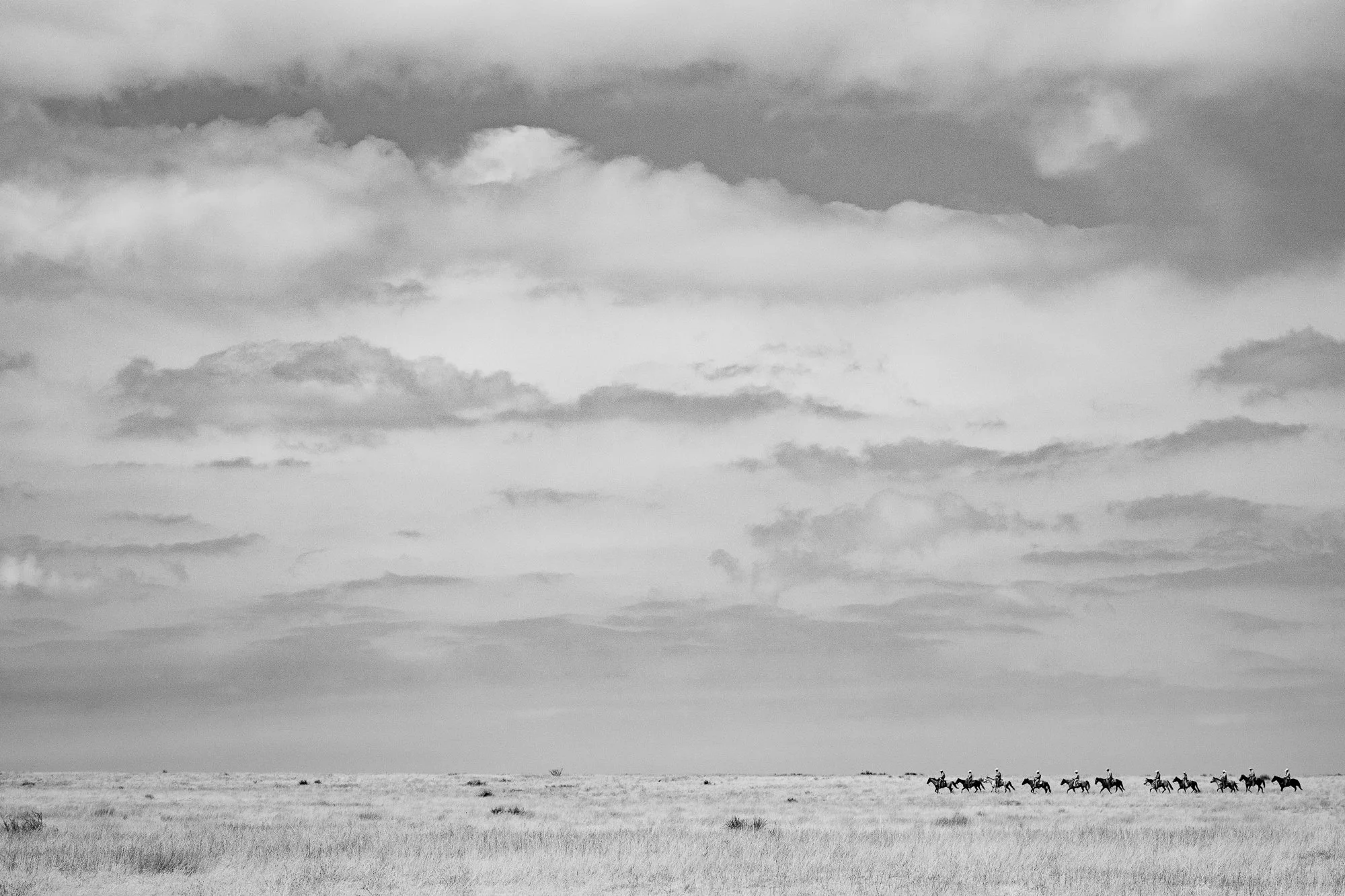 Line of cowboys riding across open prairie at the 6666 Ranch in Texas under expansive skies.