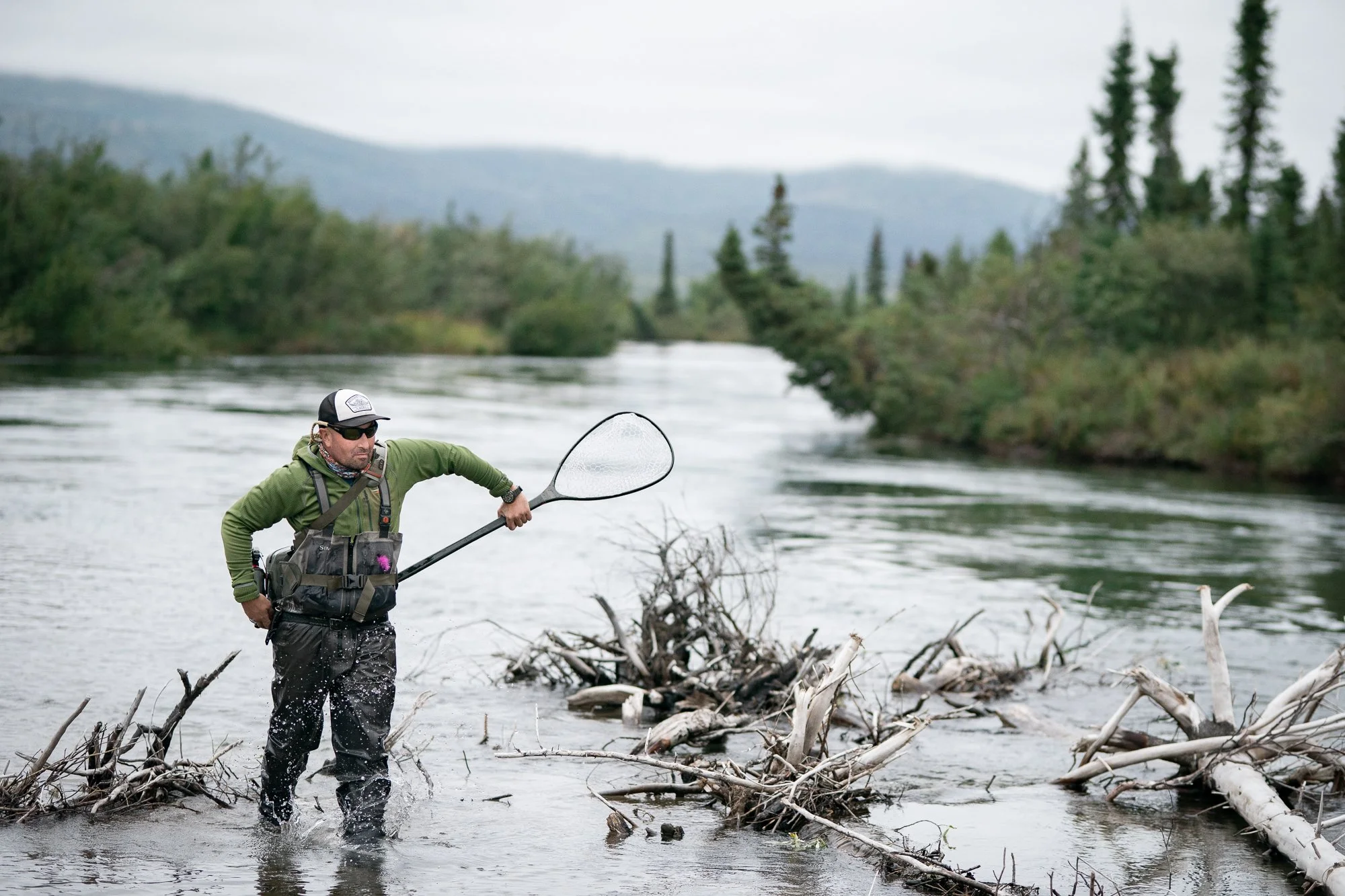 Fly fishing guide standing in an Alaskan river with a landing net