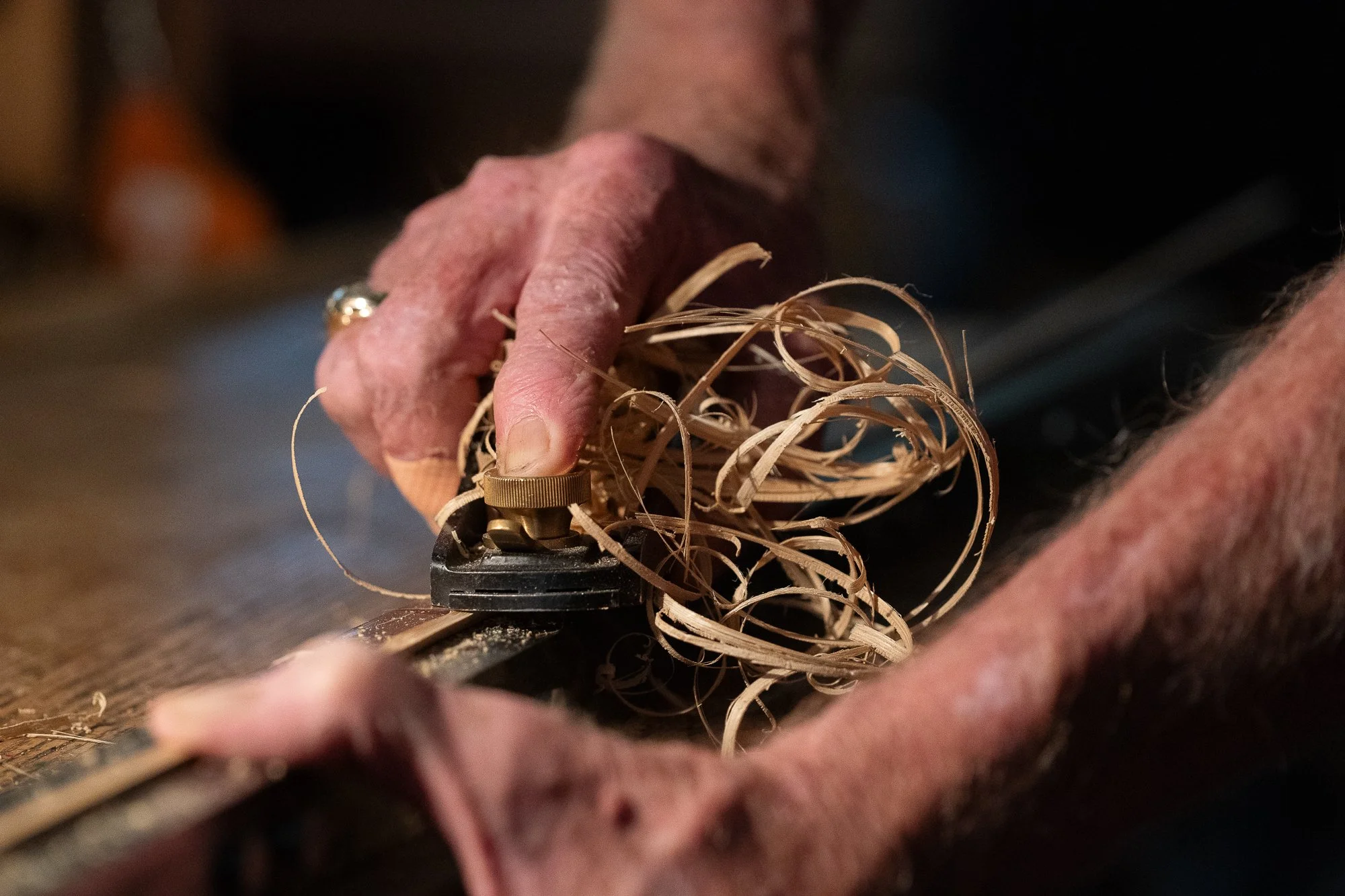 Mike Clark's hands using a plane on bamboo with curled cane shavings surrounding the tool.