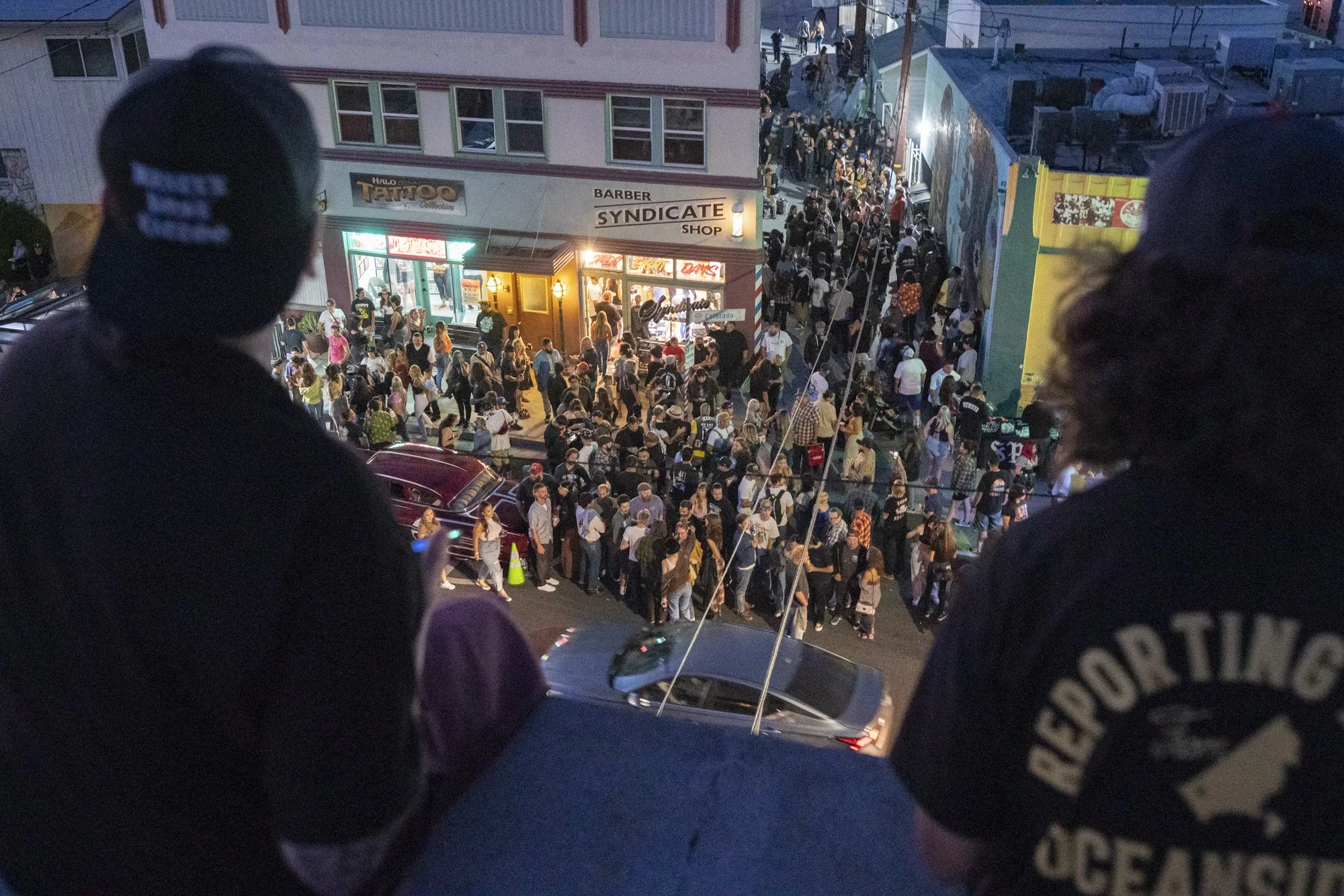 Aerial view looking down at a massive crowd filling the street in front of Syndicate Barber Shop during the 20th anniversary celebration at night