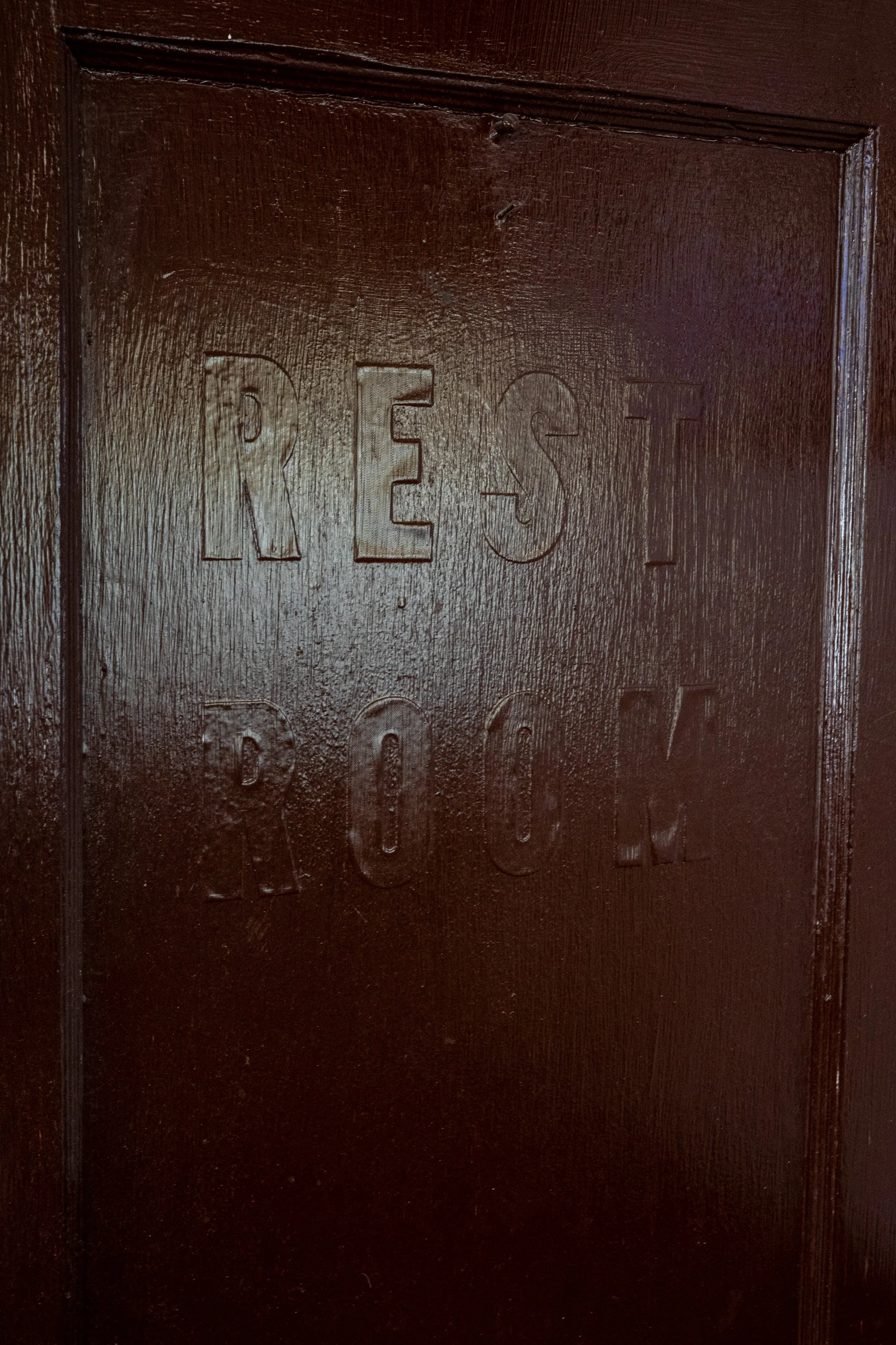 Dark wooden door embossed with the words REST ROOM inside the College Inn in Douglas, Wyoming.