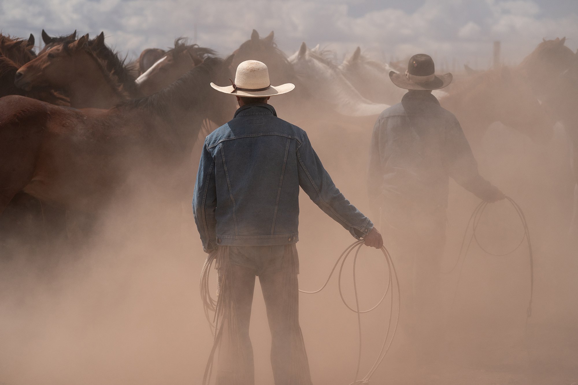 Western ranch photograph of cowboys holding ropes among horses and dust
